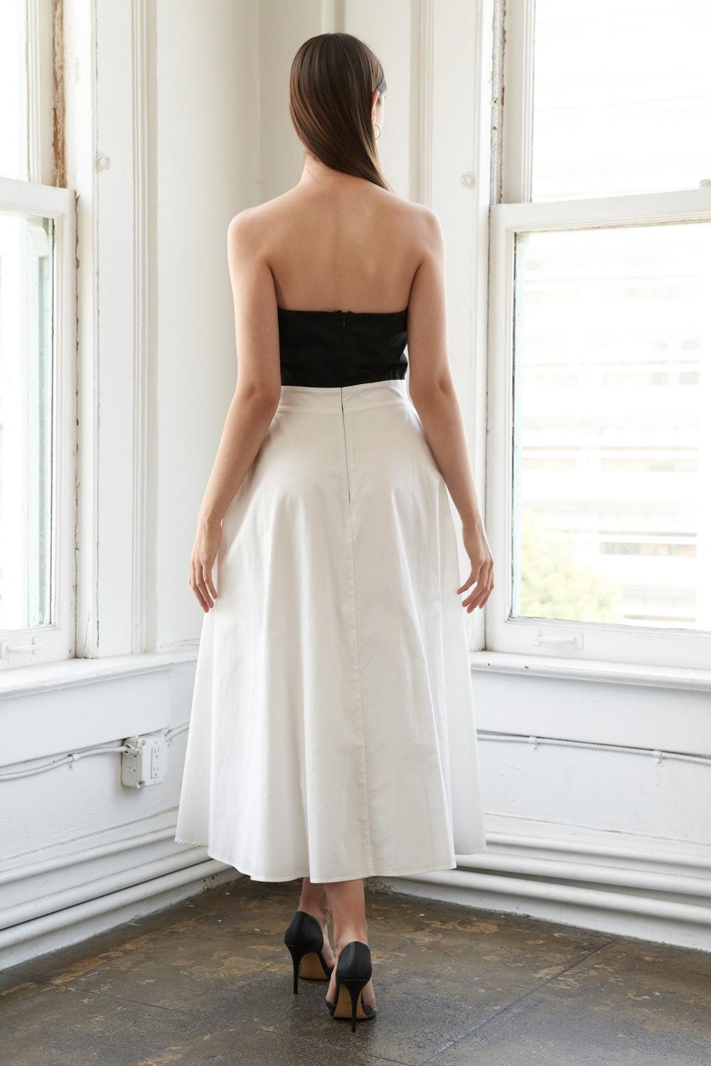 A solid woven midi dress featuring strapless top with bow, full skirt and back zipper closure