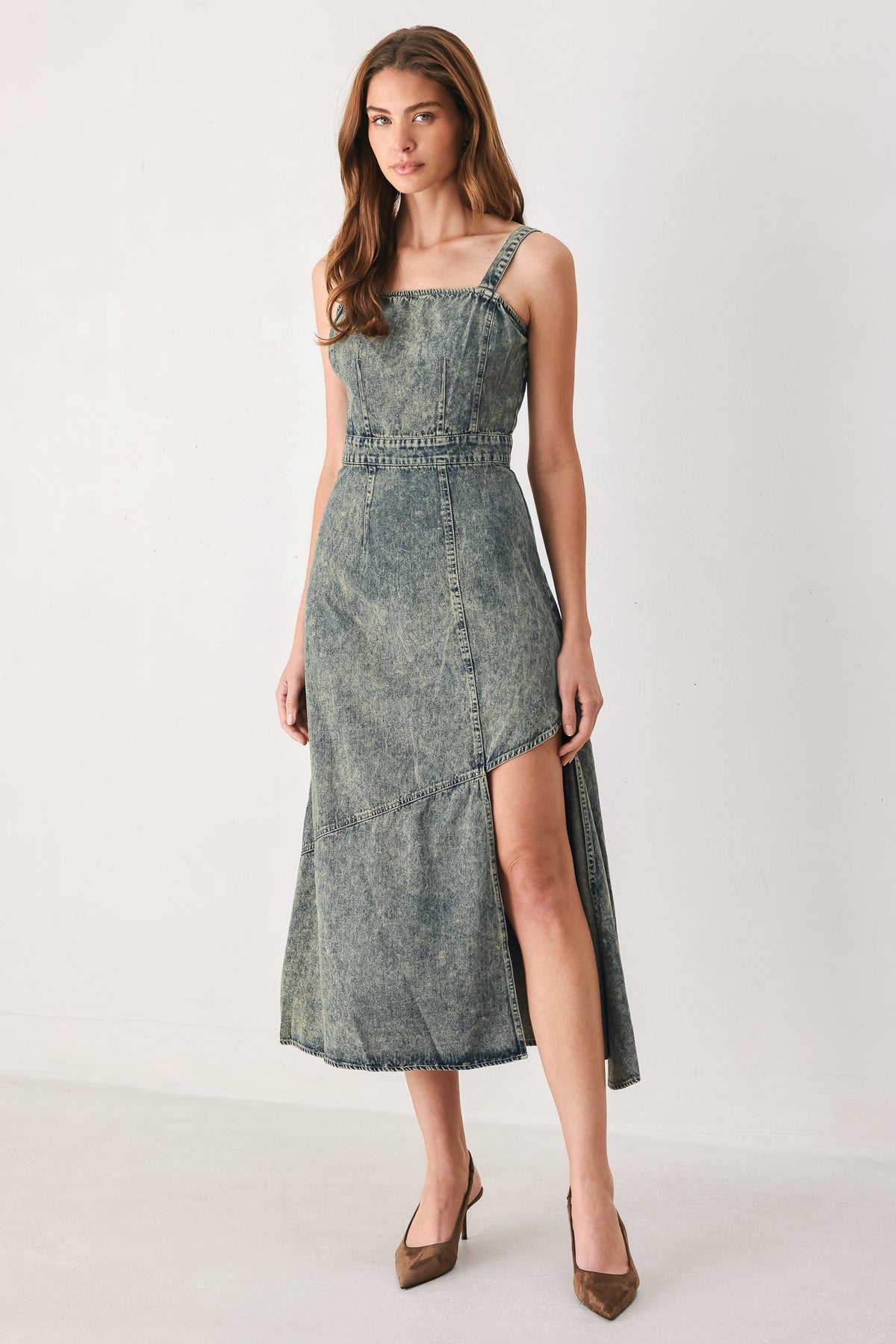 A woman modeling a sleeveless, mid-length denim dress with a distressed denim acid-wash finish, featuring a high side slit and brown pointed-toe heels | FREEMARKET