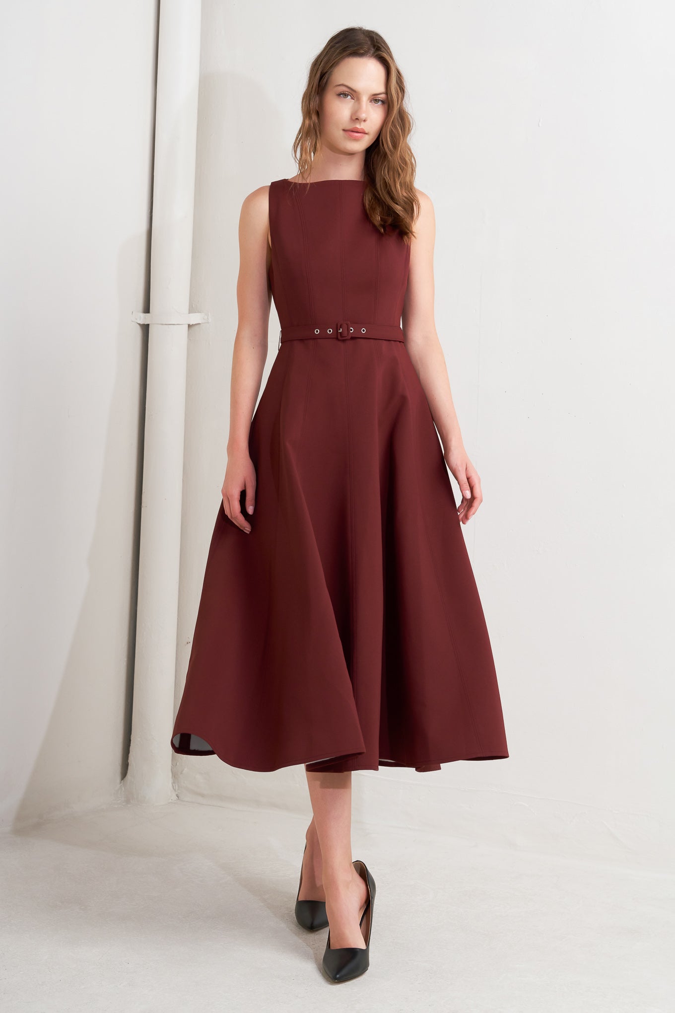 A solid woven midi dress featuring boat neckline, sleeveless, full skirt, self belt, side pocket and full skirt