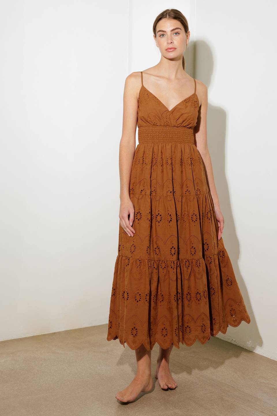 A woven eyelet midi dress featuring surplice cami top with adjustable straps, smocked waistband and tiered skirt