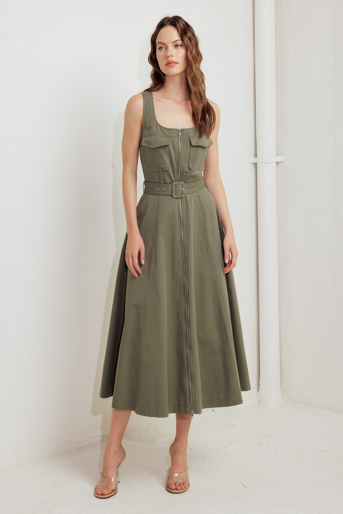 A solid woven midi dress featuring square neckline, sleeveless, front pockets, zipper closure, self belt and circle skirt