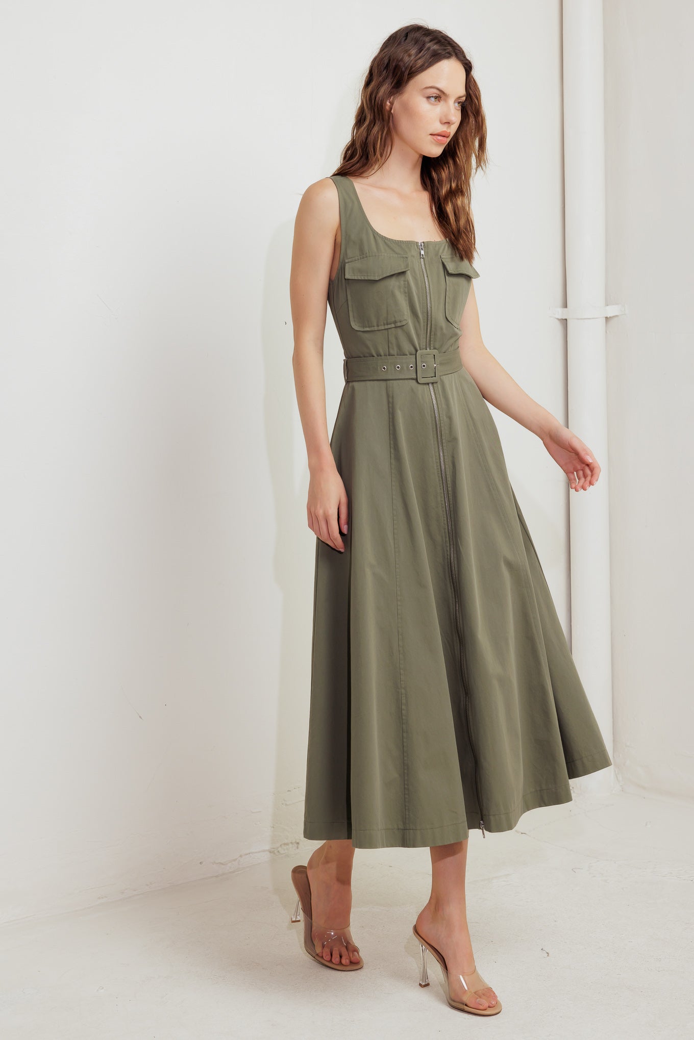 A solid woven midi dress featuring square neckline, sleeveless, front pockets, zipper closure, self belt and circle skirt