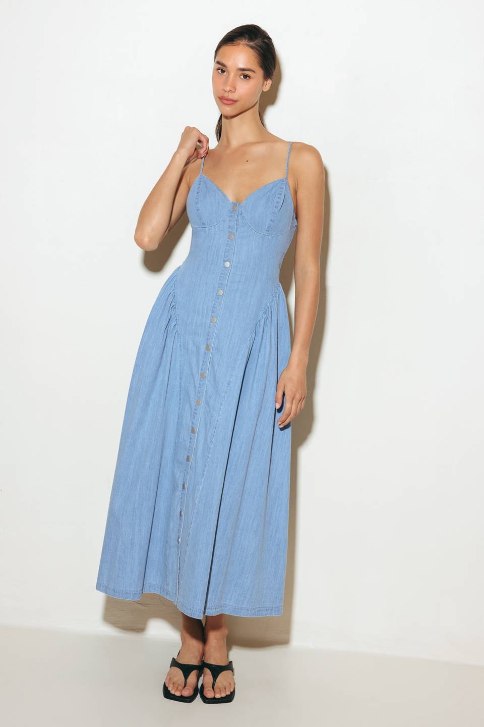 A solid lightweight denim midi dress featuring cami top, straps, button down, side shirring detail, full skirt and backside smocked detail