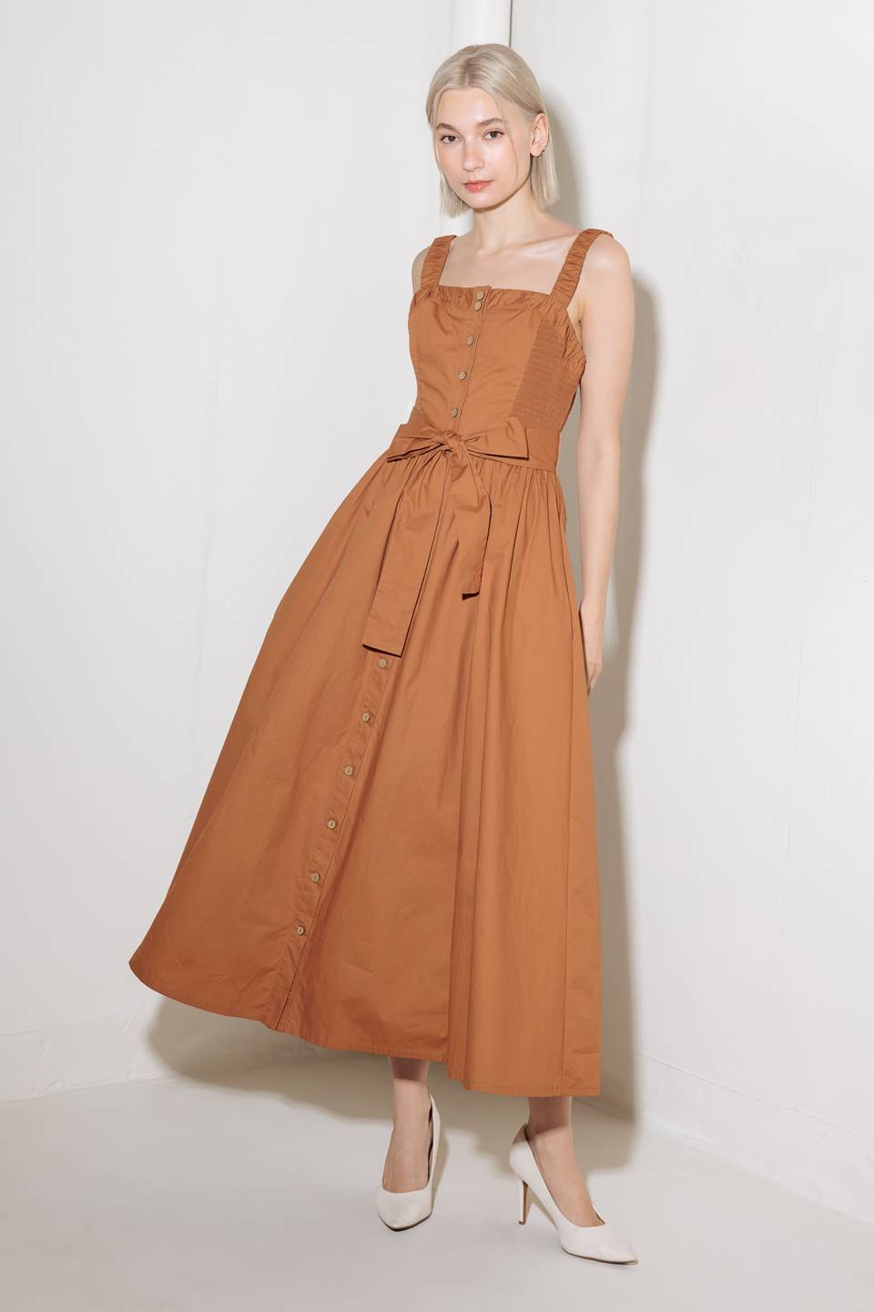 A solid woven midi dress featuring straight neckline, straps, side smocking, self sash tie and full skirt.