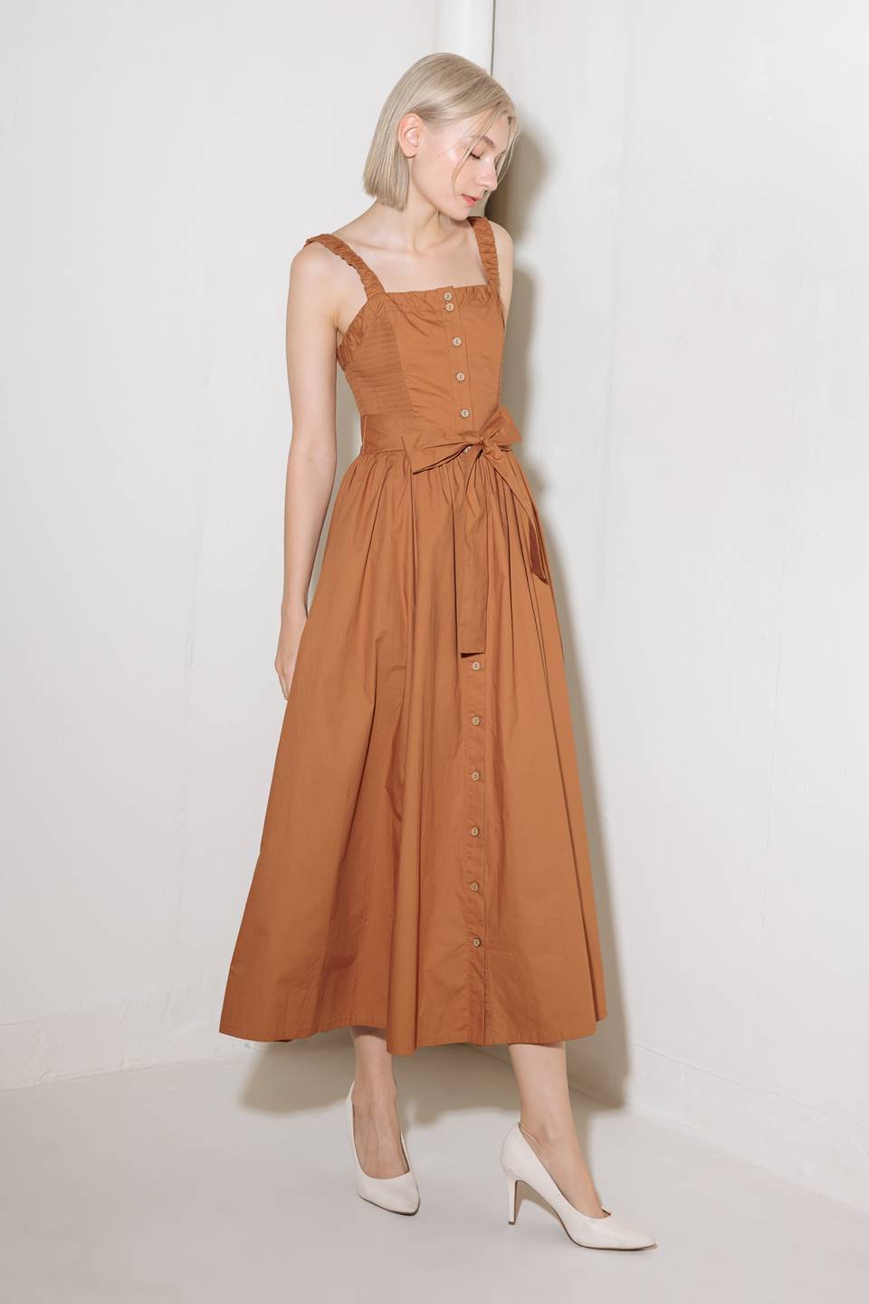 A solid woven midi dress featuring straight neckline, straps, side smocking, self sash tie and full skirt.