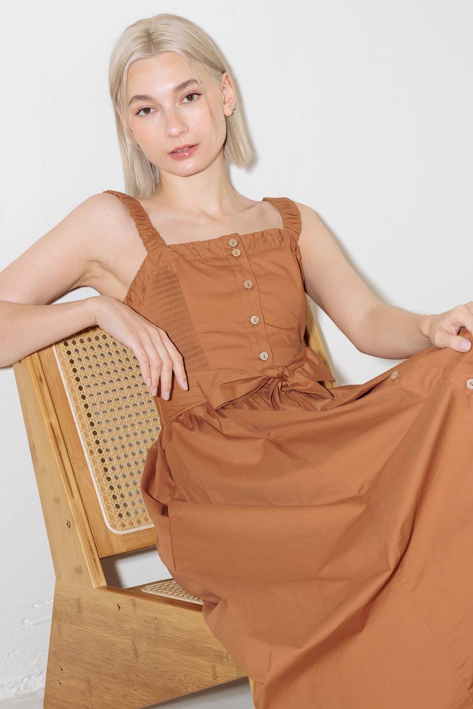 A solid woven midi dress featuring straight neckline, straps, side smocking, self sash tie and full skirt.