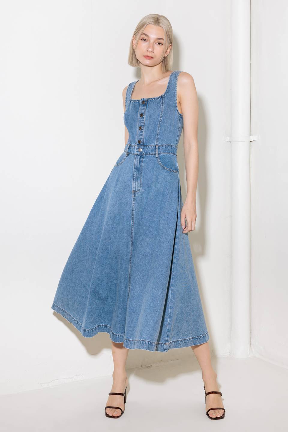 A washed denim midi dress featuring square neckline, sleeveless, front button down and zipper closure, side/back pockets and circle skirt.