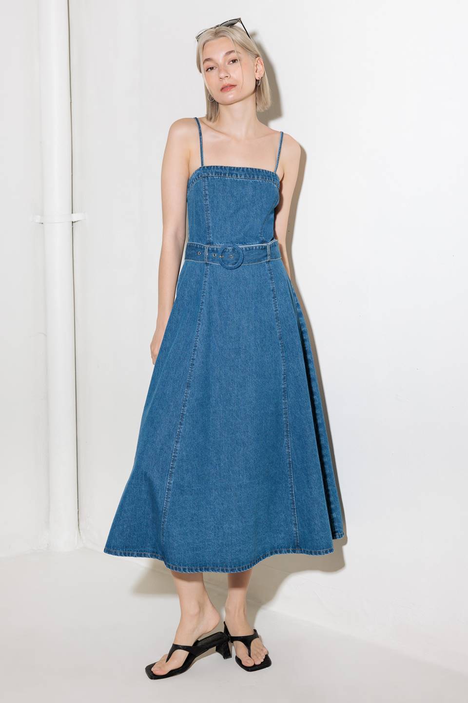 A washed denim midi dress featuring straight neckline, strap, self belt, full skirt and back zipper closure.