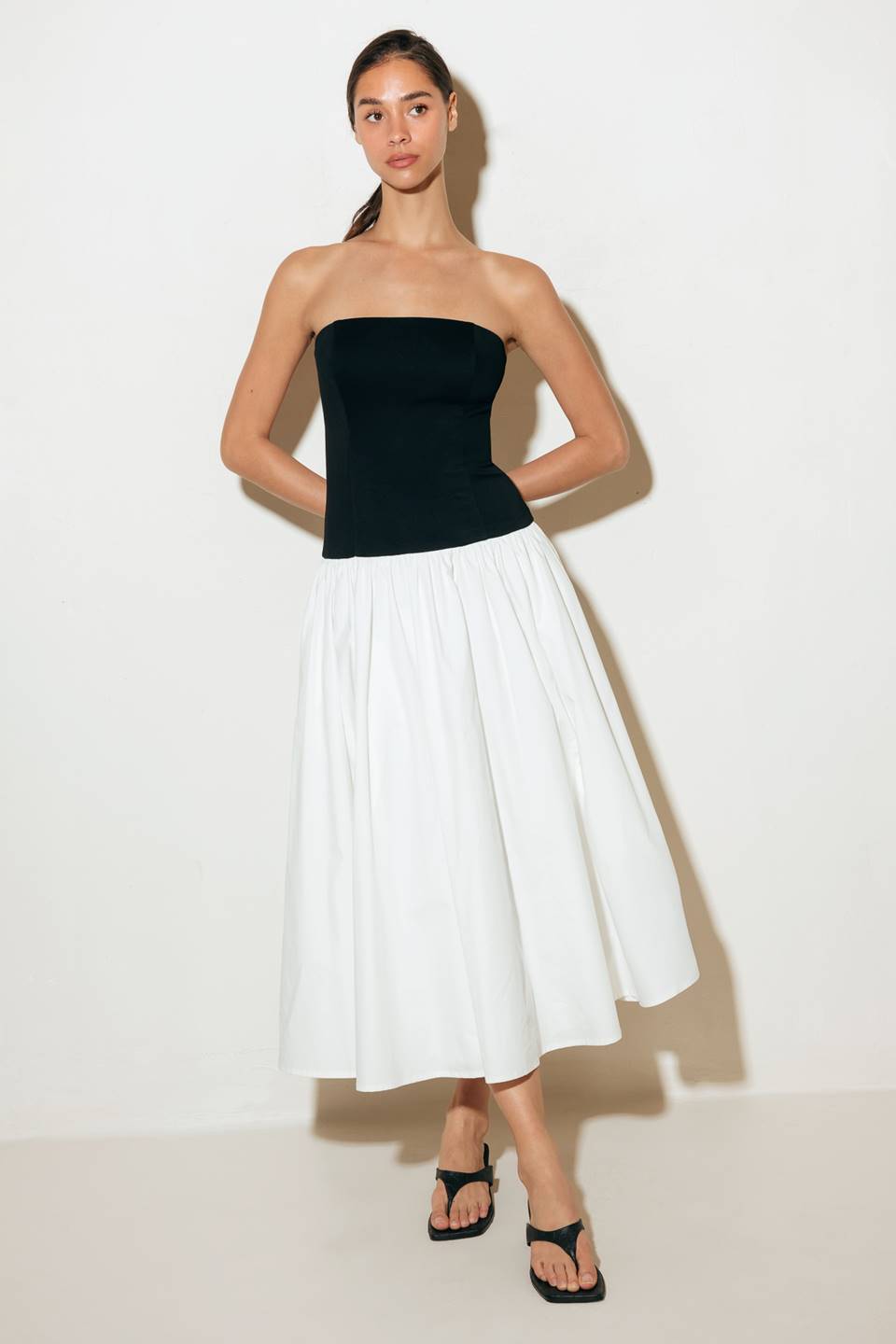 A strapless, solid black and white midi dress featuring a knit bodice, a full woven skirt, and a back zipper closure.