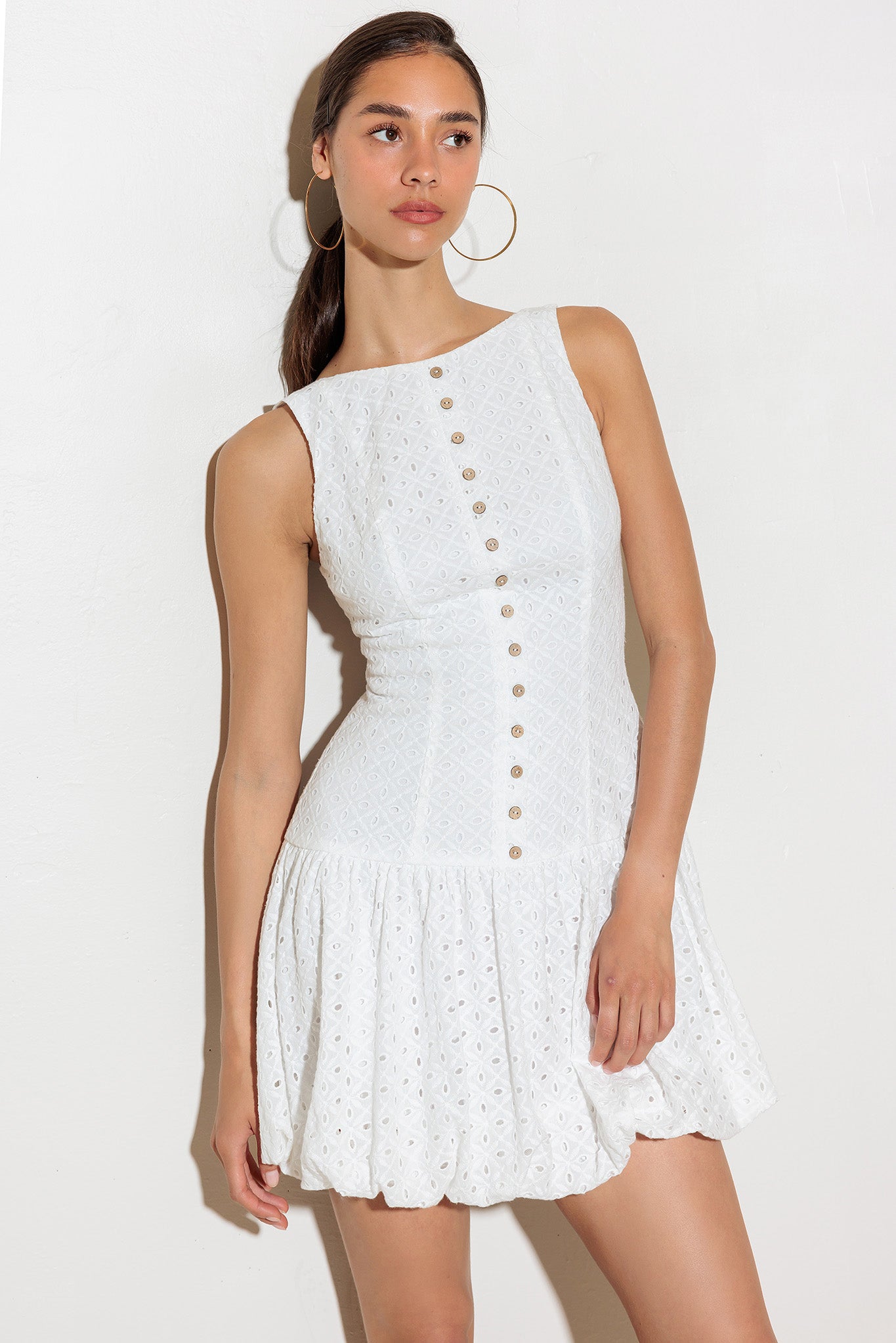 An eyelet textured woven mini dress featuring round neckline, sleeveless, dropped waist, full skirt and back zipper bow closure.