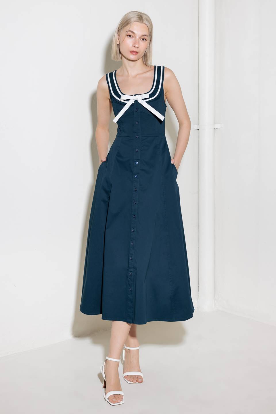 A solid woven midi dress fearturing U neckline, sleeveless, contrasting band and bow, button down and circle skirt.