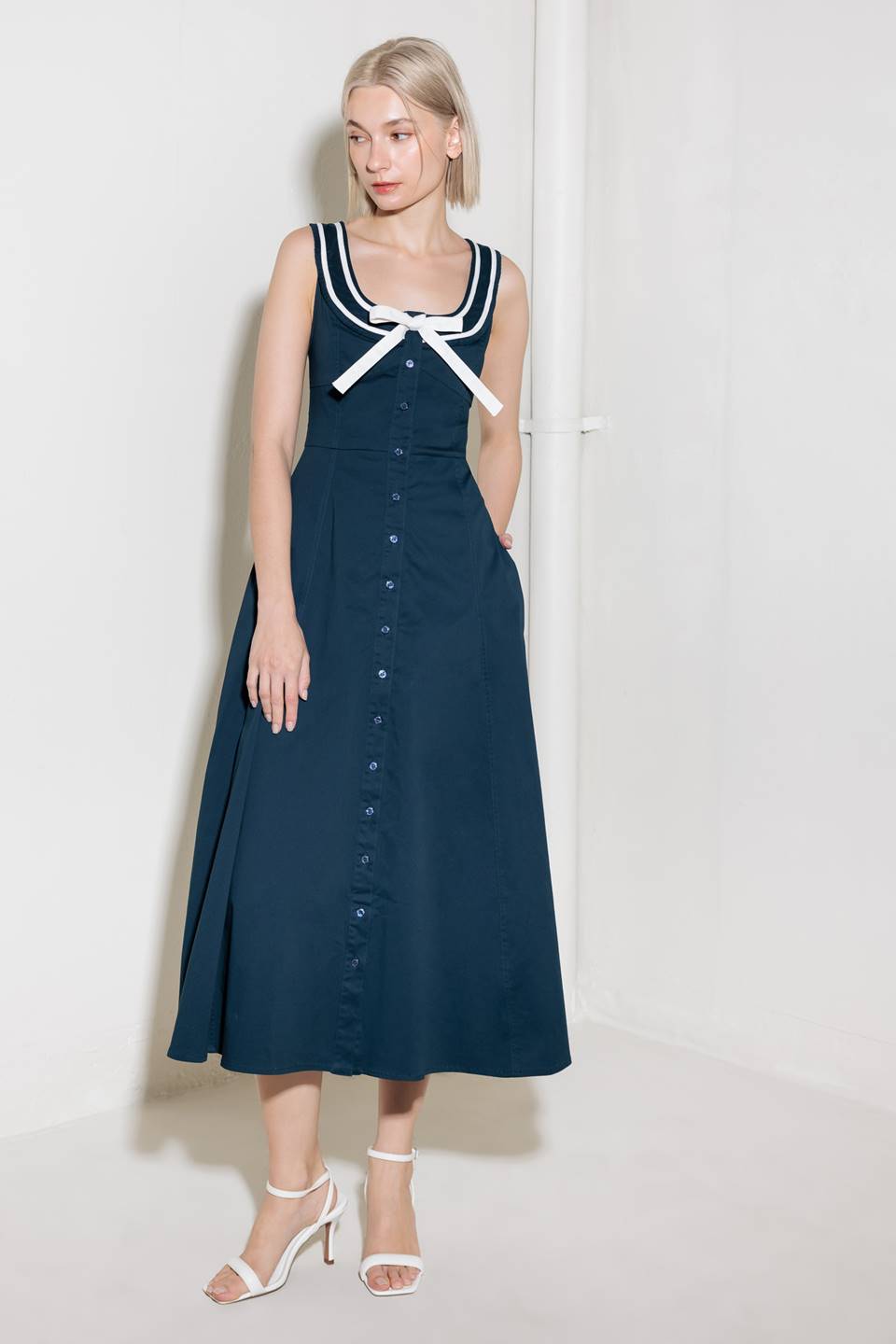 A solid woven midi dress fearturing U neckline, sleeveless, contrasting band and bow, button down and circle skirt.