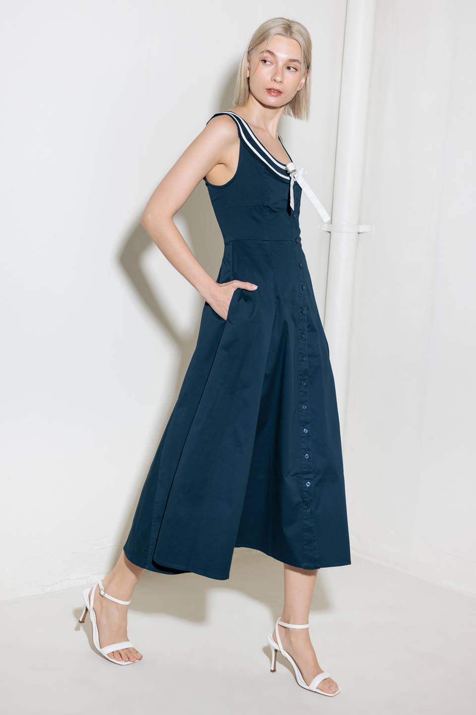 A solid woven midi dress fearturing U neckline, sleeveless, contrasting band and bow, button down and circle skirt.