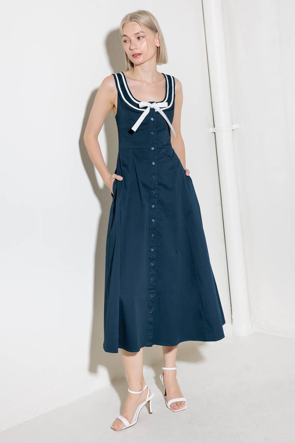 A solid woven midi dress fearturing U neckline, sleeveless, contrasting band and bow, button down and circle skirt.
