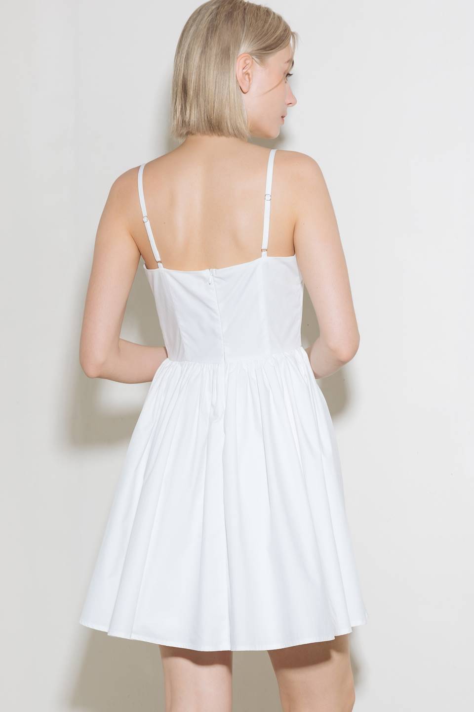 A solid woven mini dress featuring straight neckline with center V, straps, full skirt and back zipper closure.