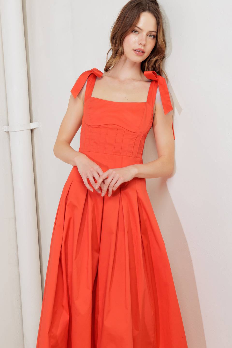 A solid red woven midi dress featuring straight neckline, shoulder ties, pintuck waist, inverted pleated skirt and bare back with straps and zipper closure
