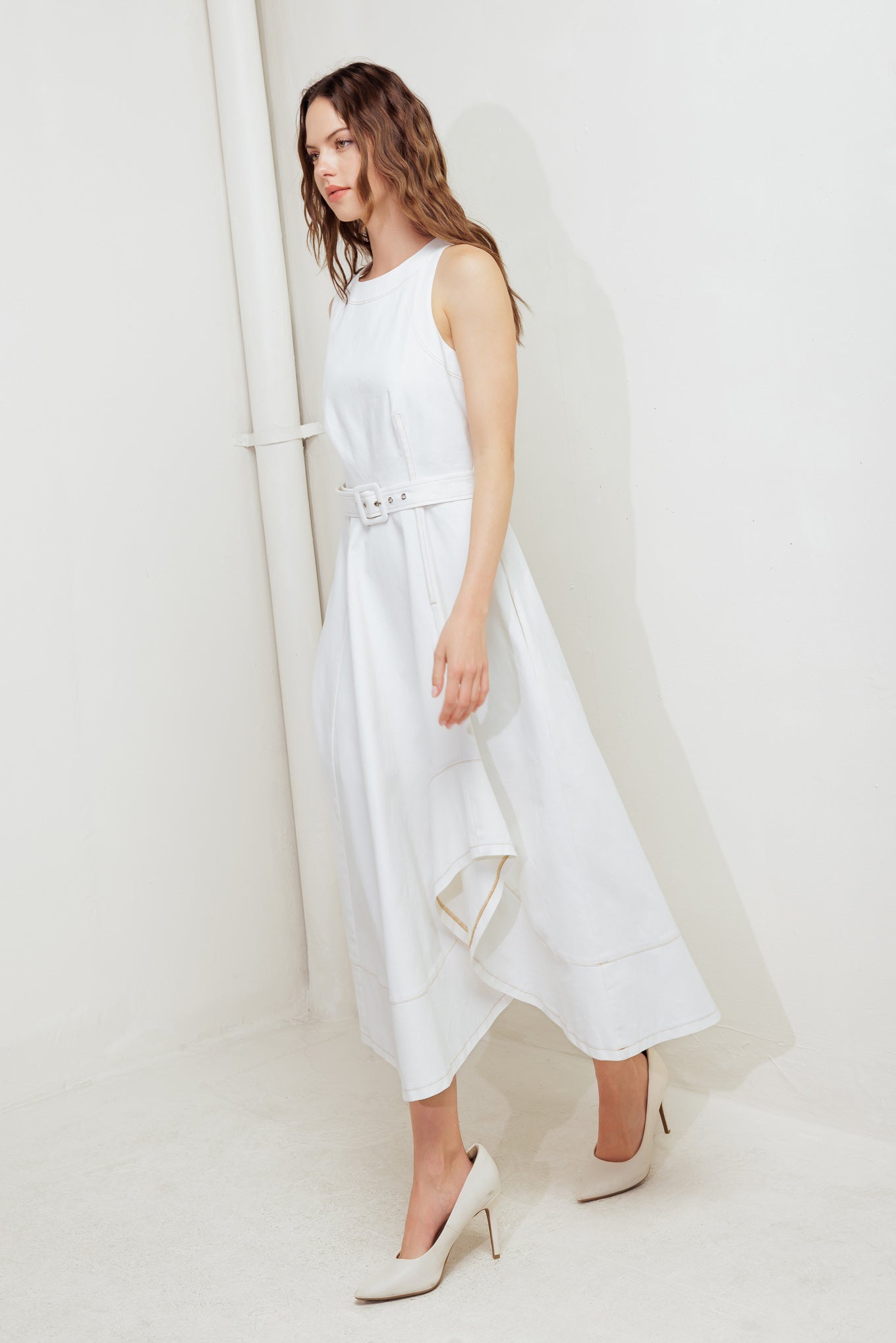 A solid white woven midi dress featuring round neckline, sleeveless, self belt, circle skirt with side hi-lo and back zipper closure