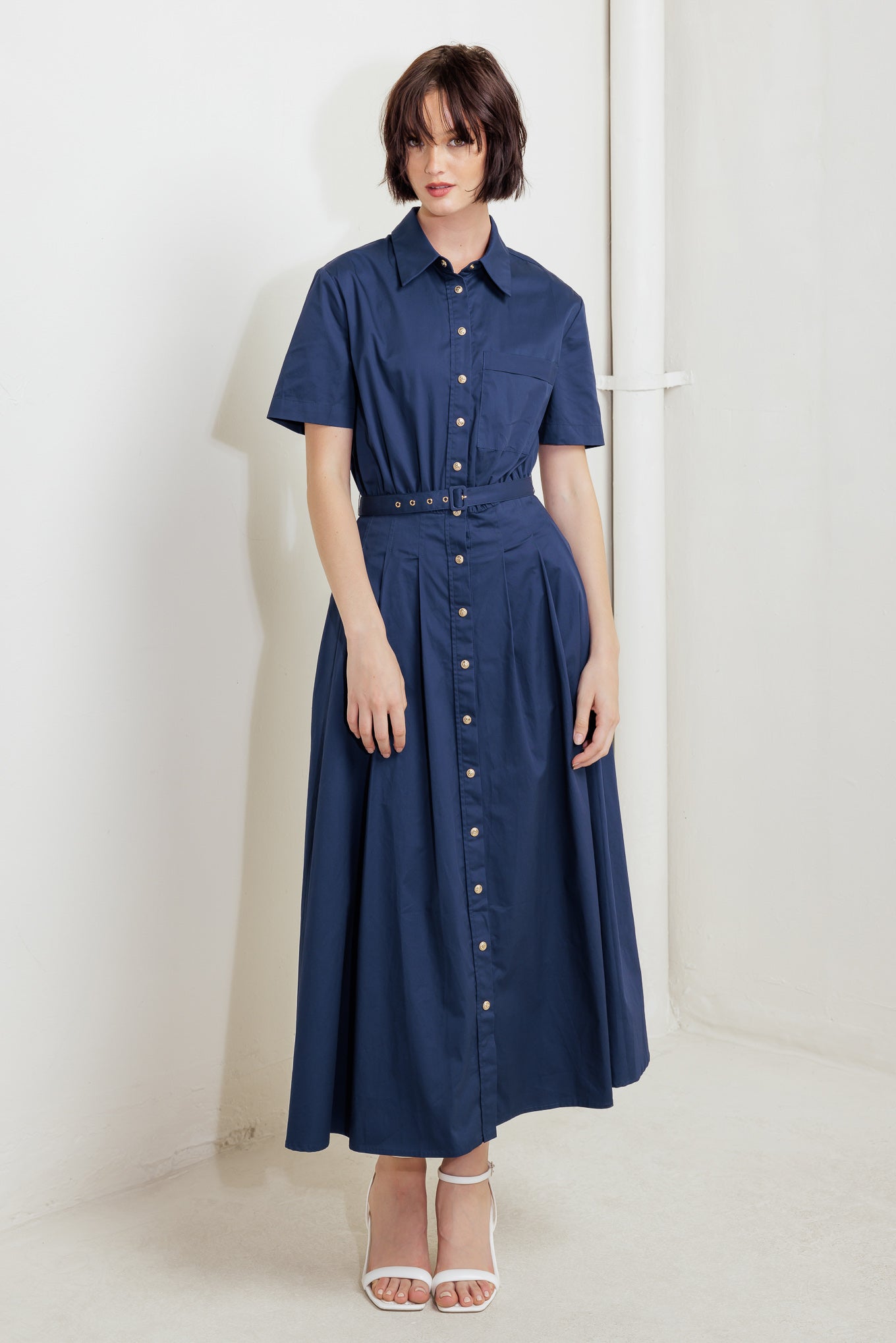 A solid woven midi dress featuring collar, short sleeve, front pocket, button down, self belt and full skirt