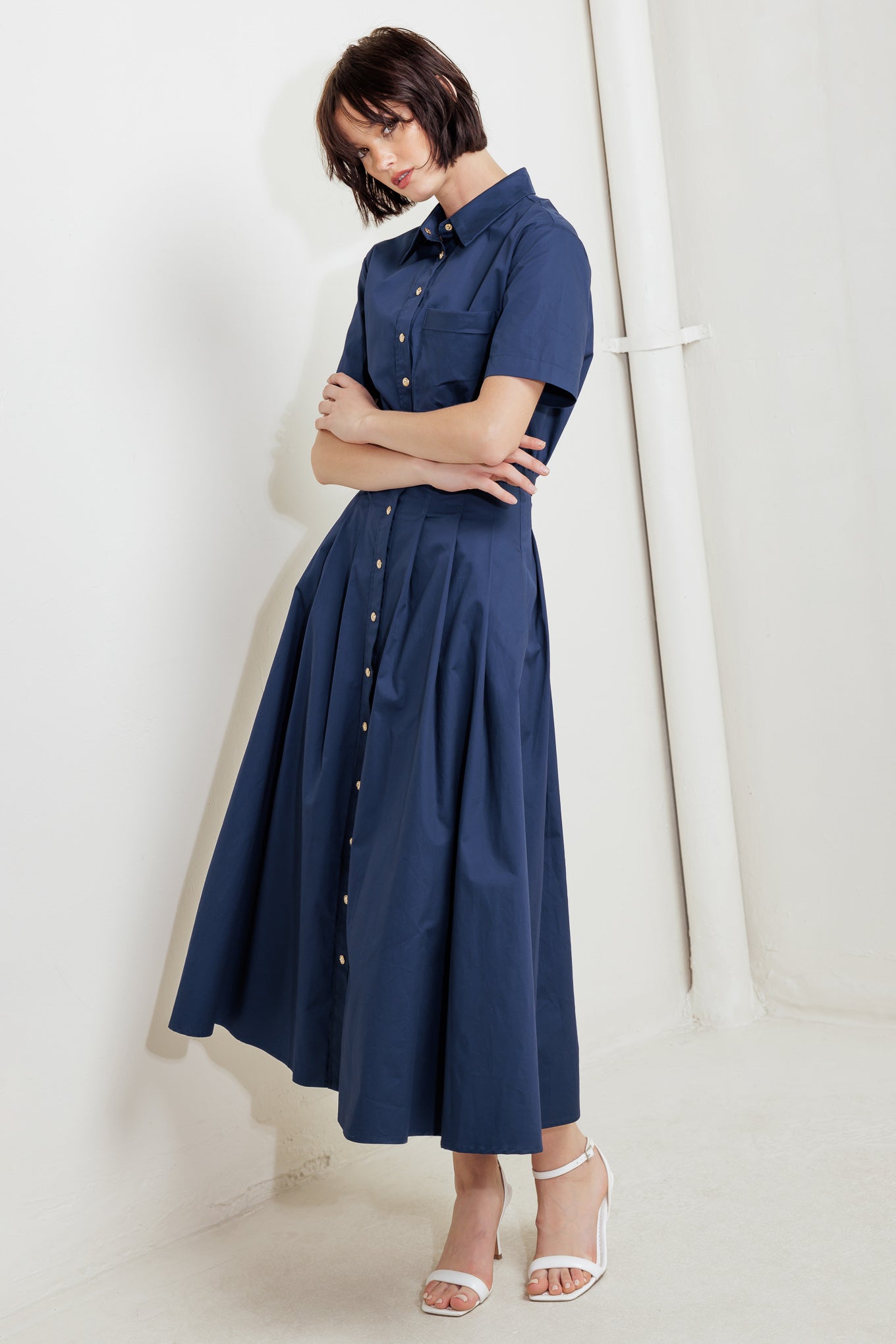 A solid woven midi dress featuring collar, short sleeve, front pocket, button down, self belt and full skirt