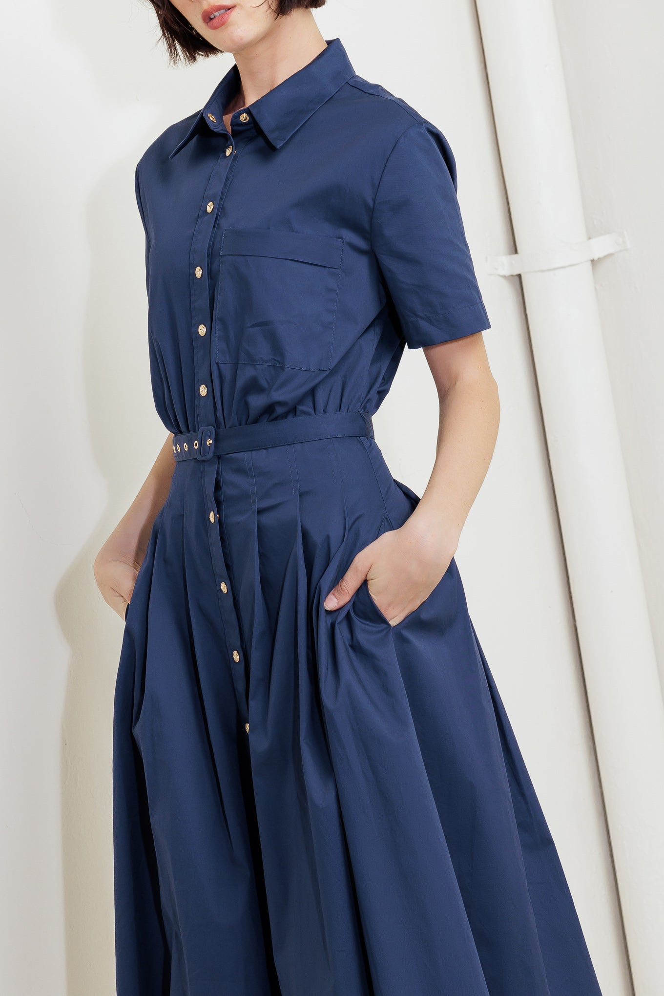 A solid woven midi dress featuring collar, short sleeve, front pocket, button down, self belt and full skirt