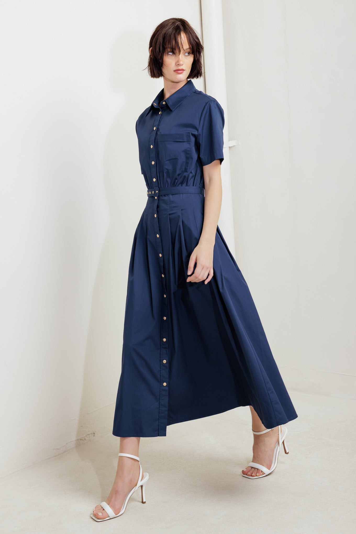 A solid woven midi dress featuring collar, short sleeve, front pocket, button down, self belt and full skirt