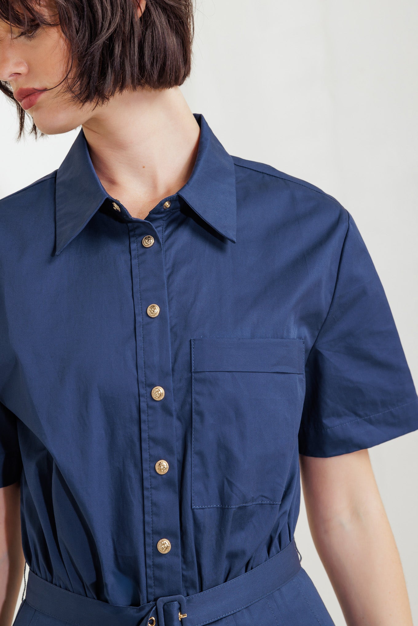 A solid woven midi dress featuring collar, short sleeve, front pocket, button down, self belt and full skirt