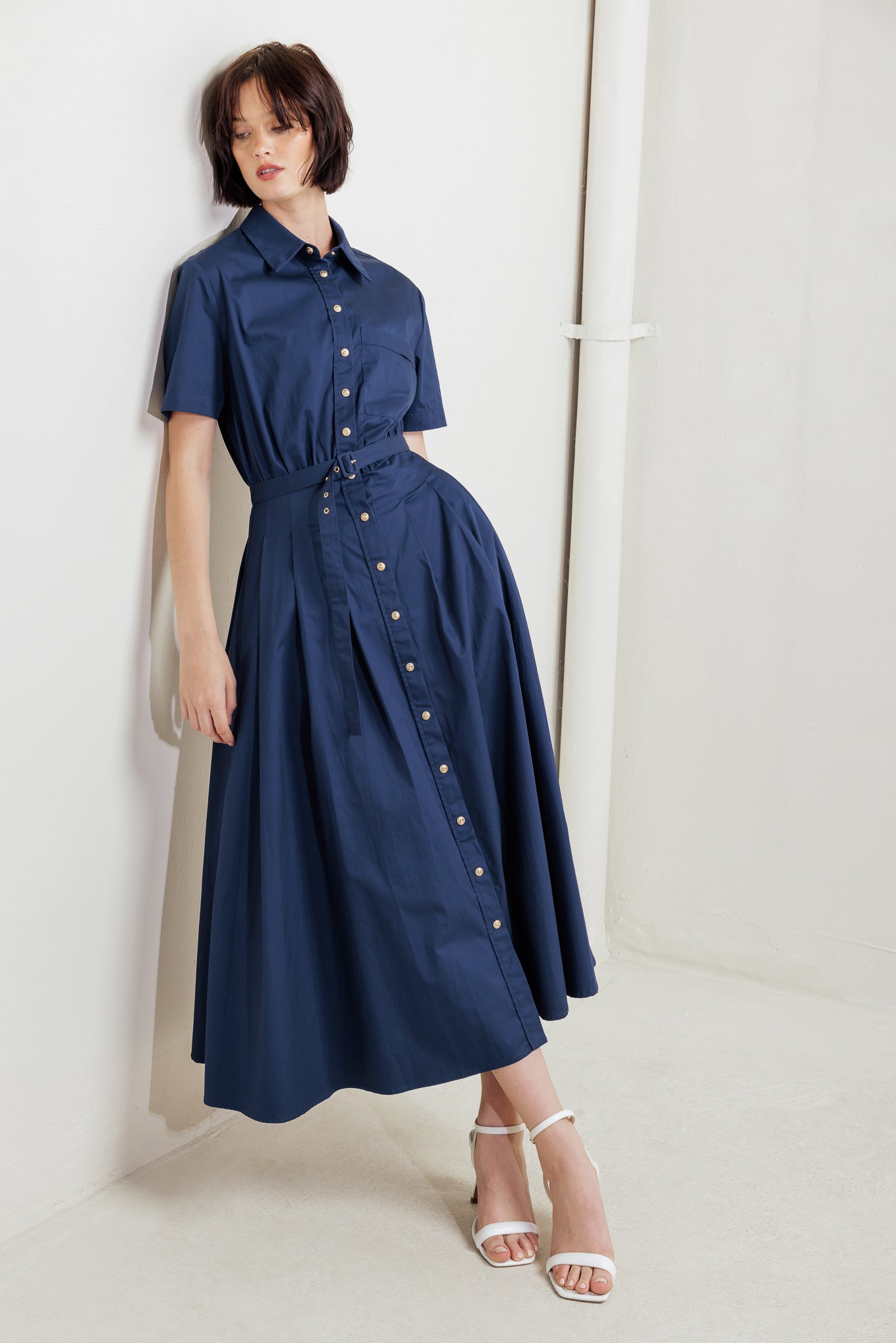 A solid woven midi dress featuring collar, short sleeve, front pocket, button down, self belt and full skirt