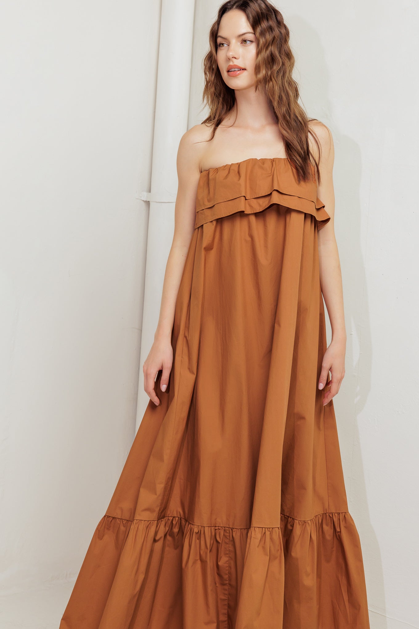 A solid woven midi dress featuring strapless with double flounce, contrasting belt and ruffled hemline