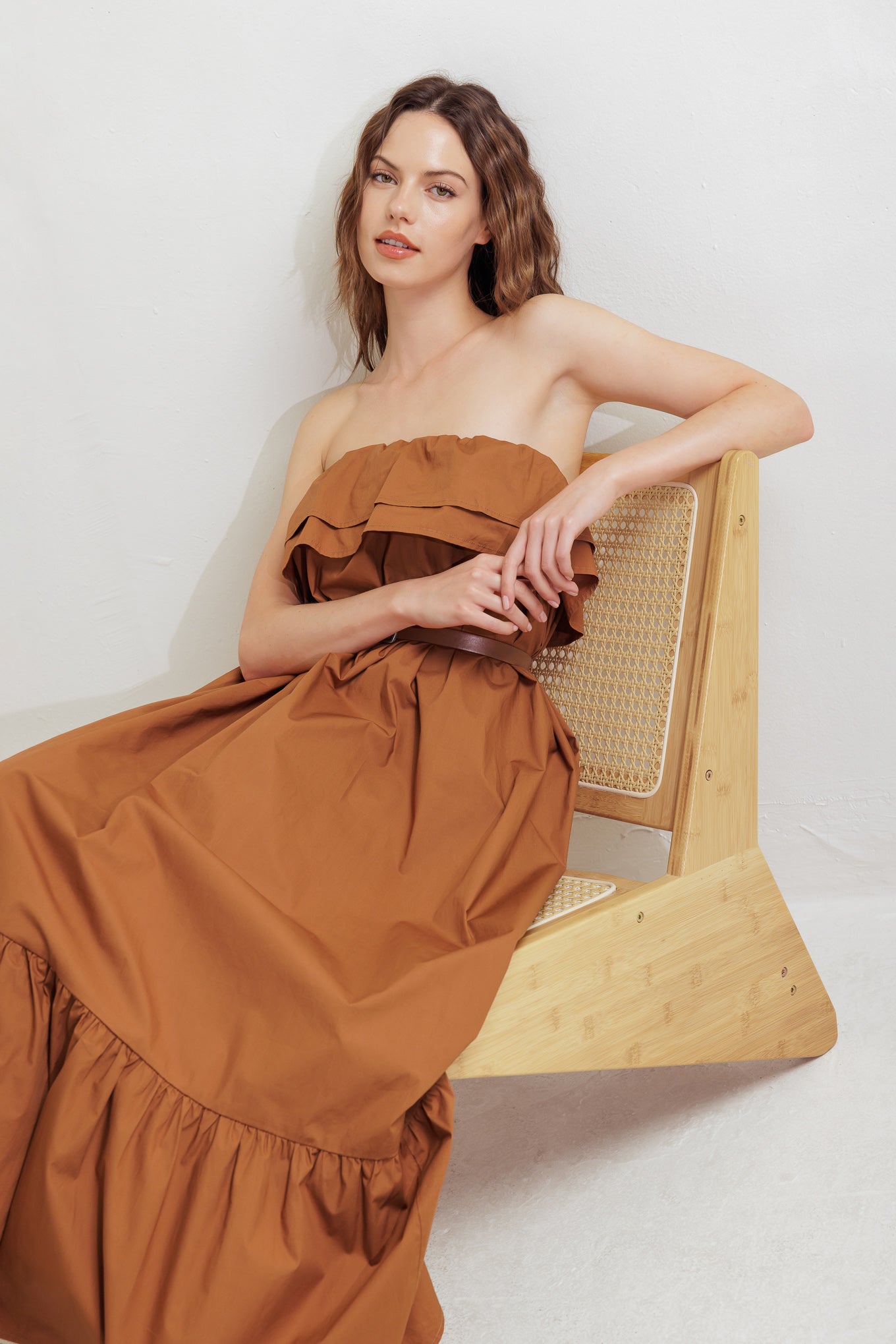 A solid woven midi dress featuring strapless with double flounce, contrasting belt and ruffled hemline