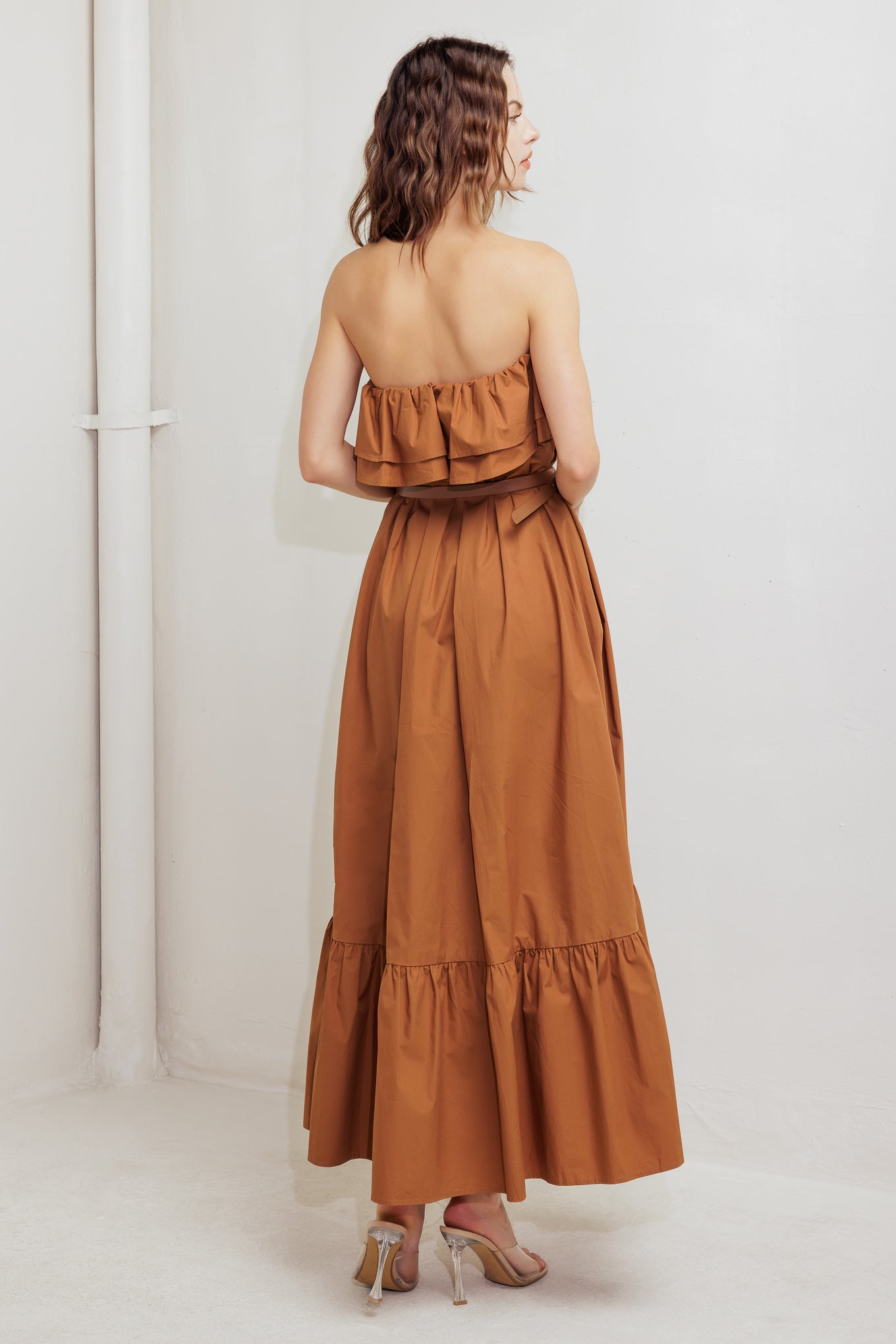 A solid woven midi dress featuring strapless with double flounce, contrasting belt and ruffled hemline