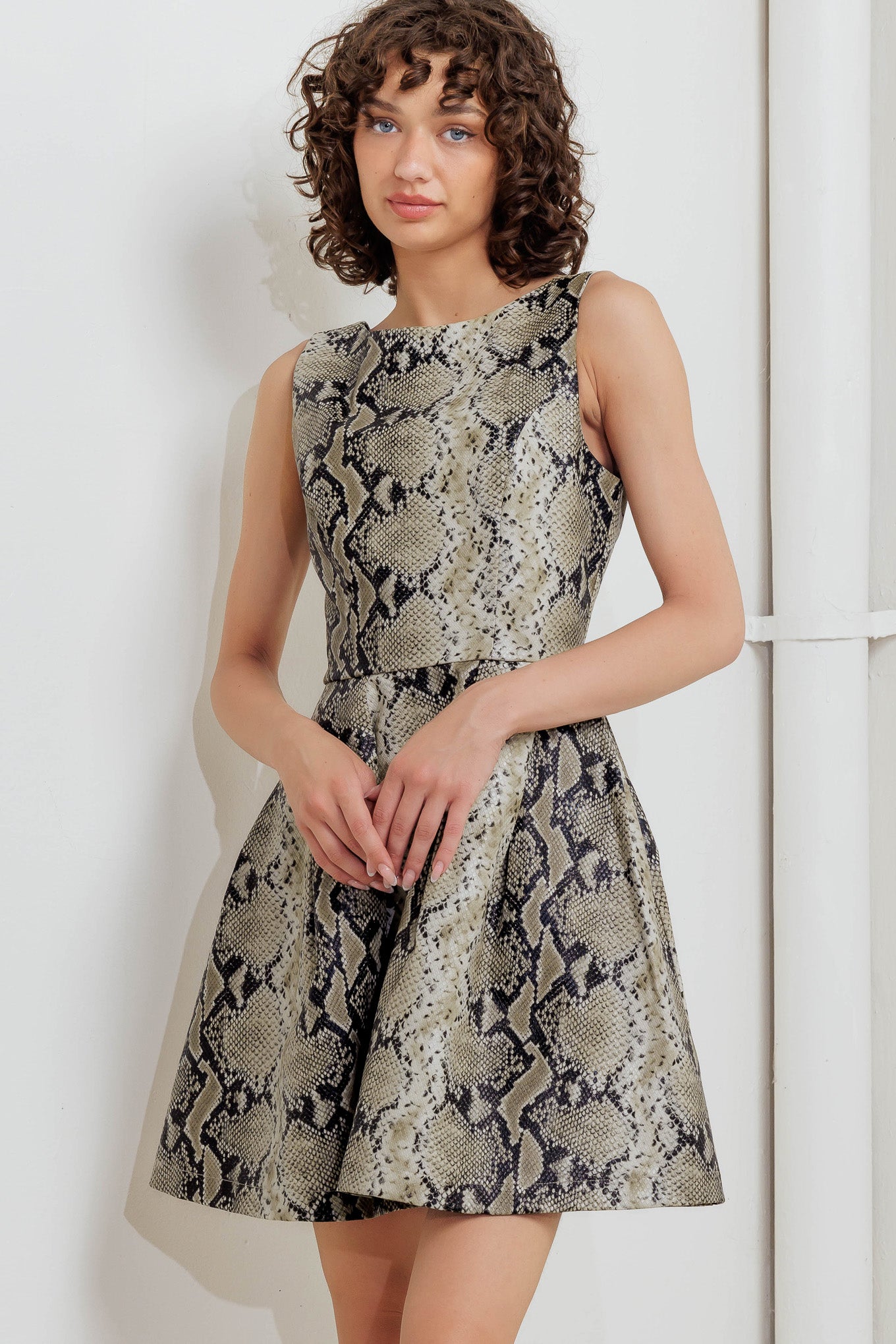 A printed faux leather mini dress featuring wide neckline, sleeveless, full skirt, U back and zipper closure