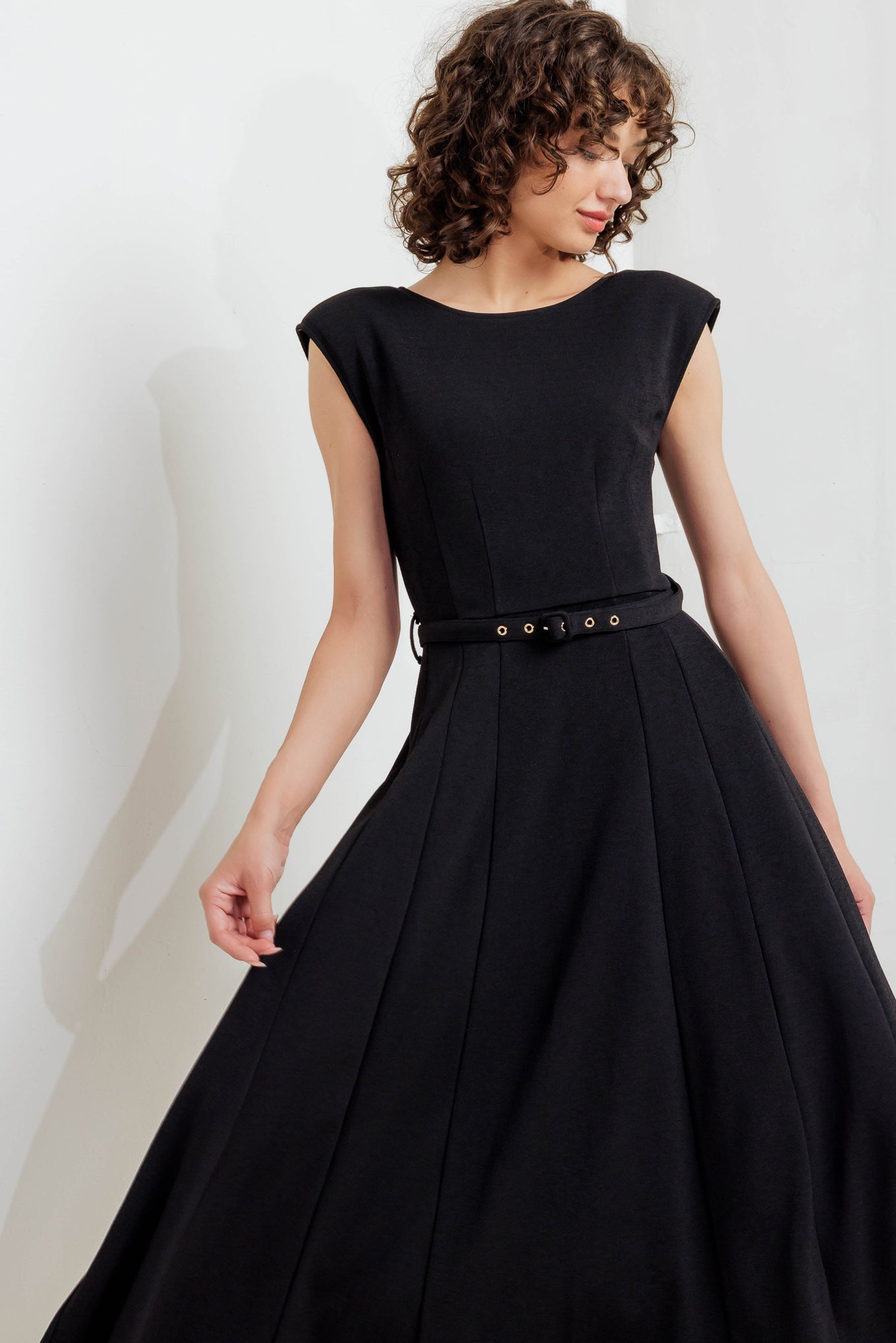 A solid woven midi dress featuring round neckline, drop shoulder, self belt, circle skirt, V back bodice and zipper closure