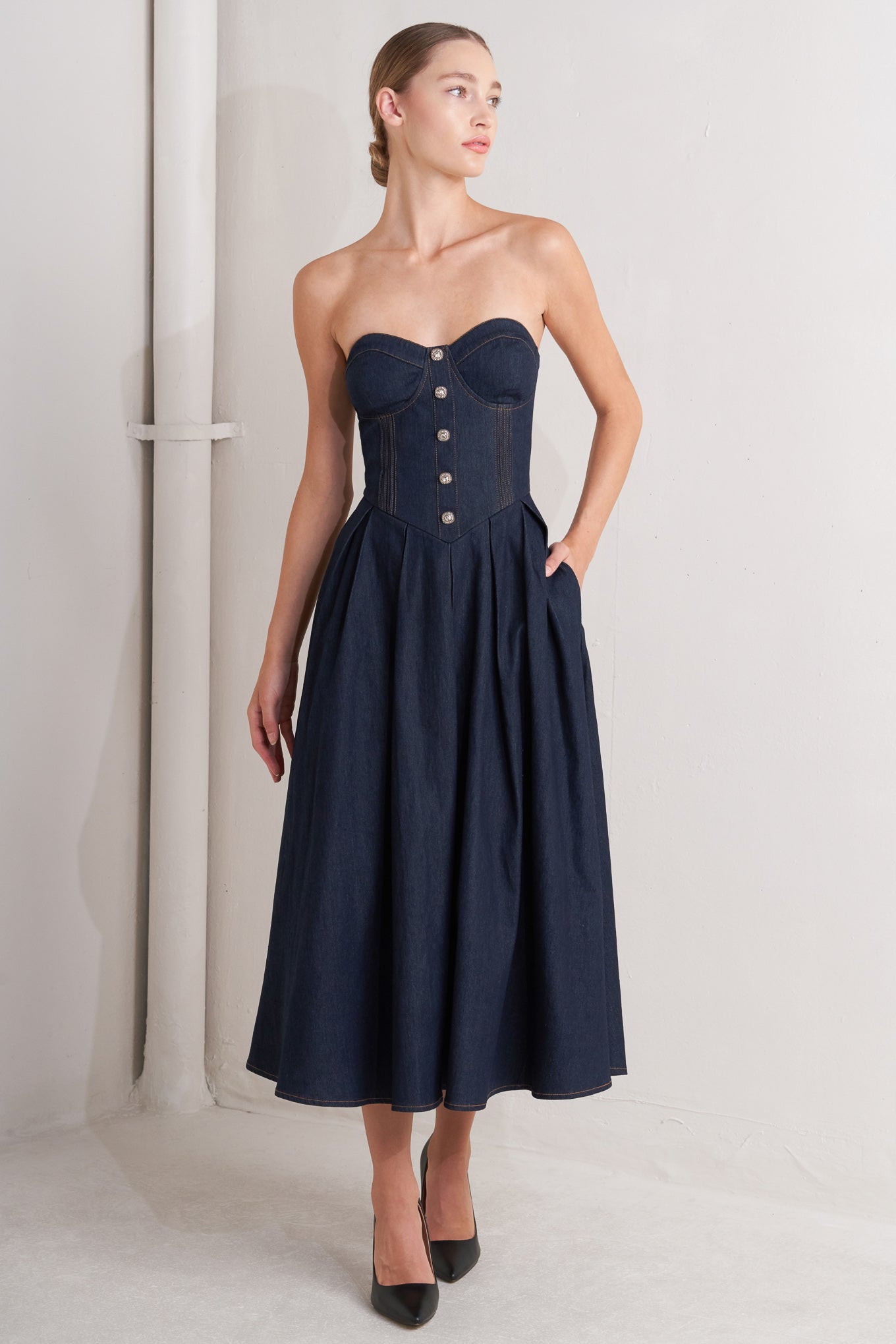 A denim midi dress featuring strapless sweetheart neckline, bustier bodice with button detail, basque waist, full skirt and back zipper closure