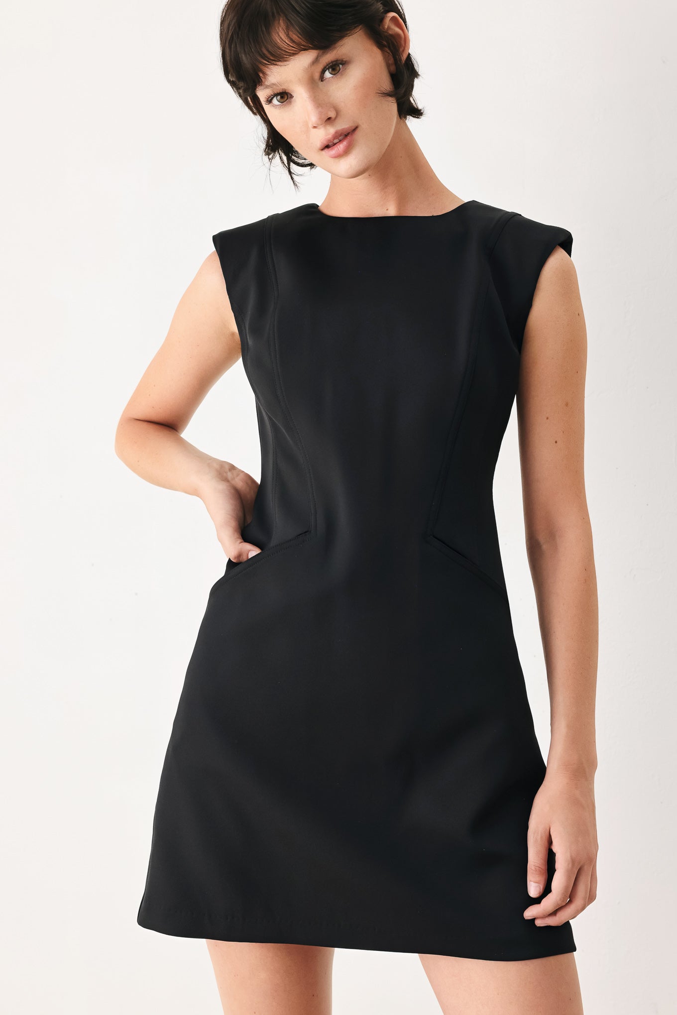 Woman wearing a black shift mini dress featuring wide round neckline, cap sleeve, pockets and back zipper closure | FREEMARKET