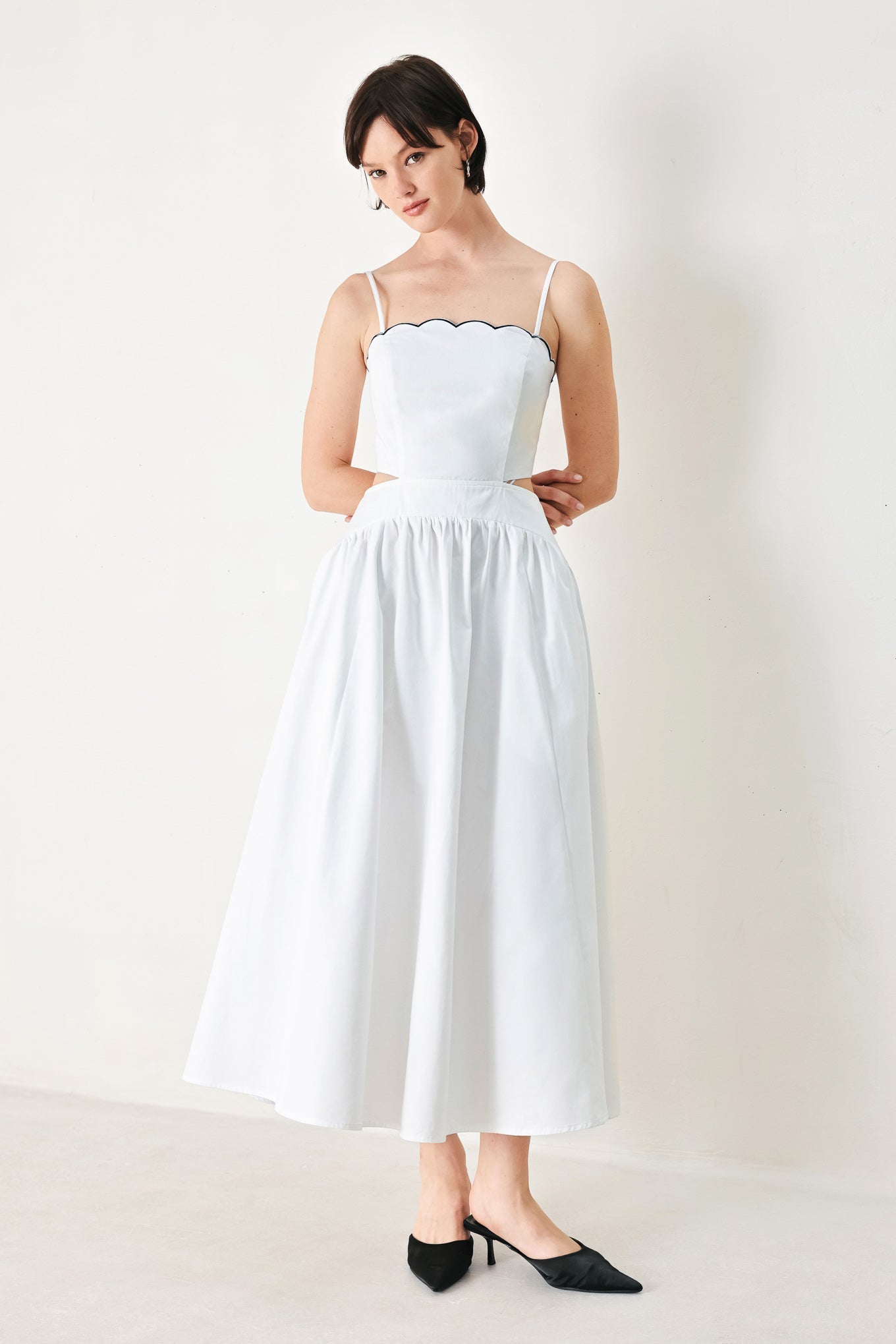 A solid woven midi dress featuring scalloped neckline, straps, side cut out, full skirt, smocked back bodice with zipper closure