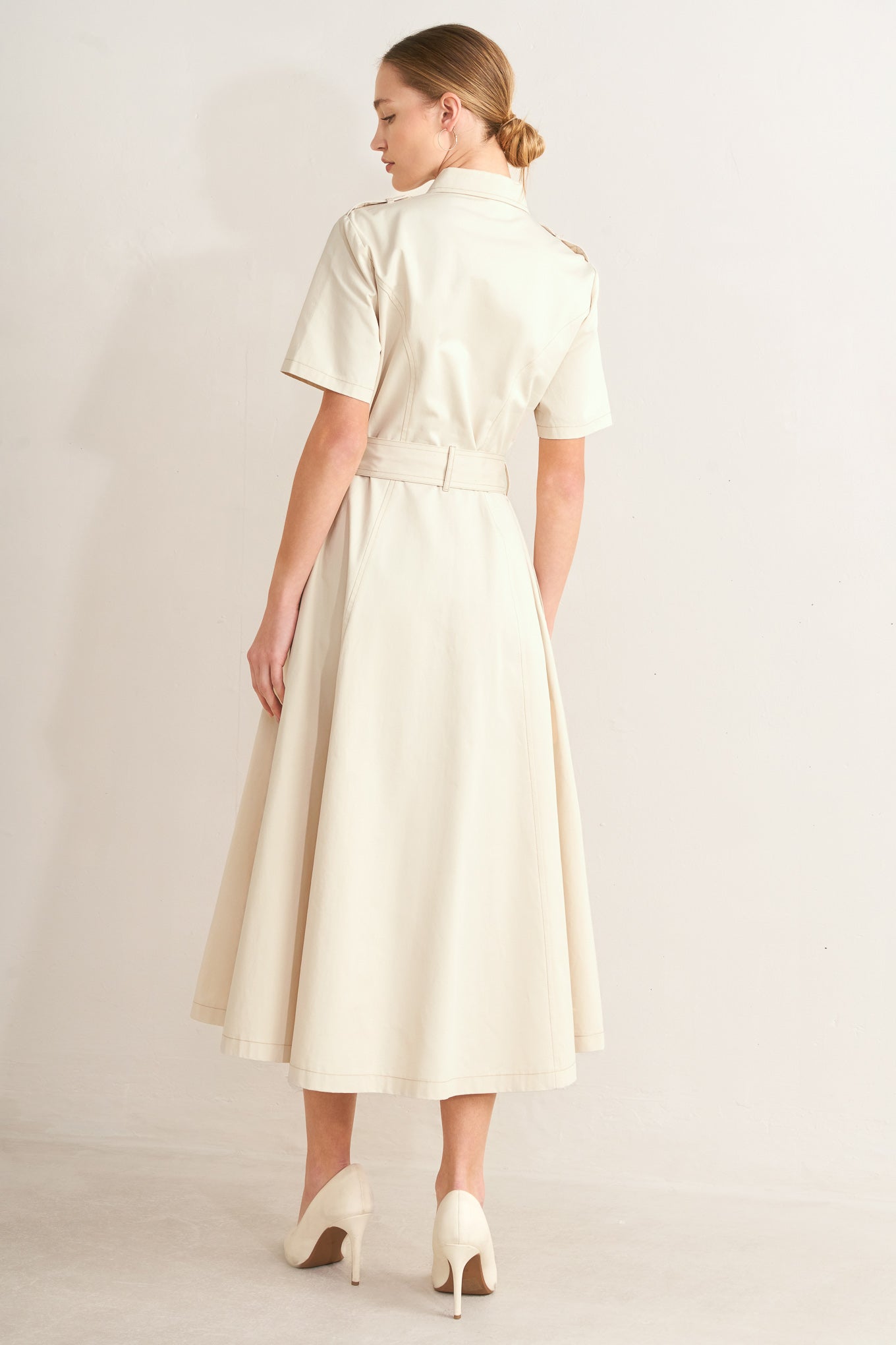 Woman wearing a cream-colored dress with a belt on a plain background
