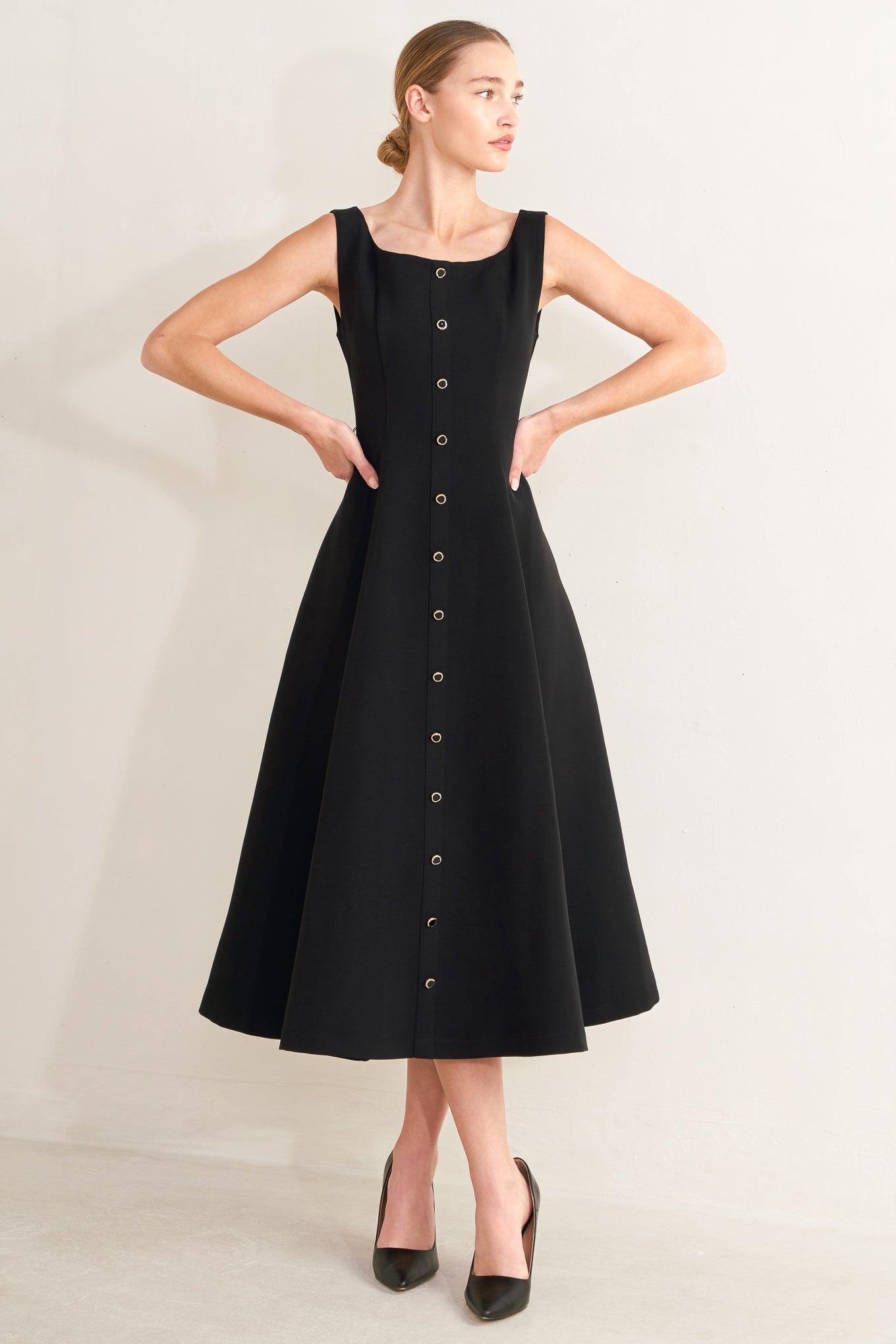 Woman wearing a black dress with buttons on a plain background