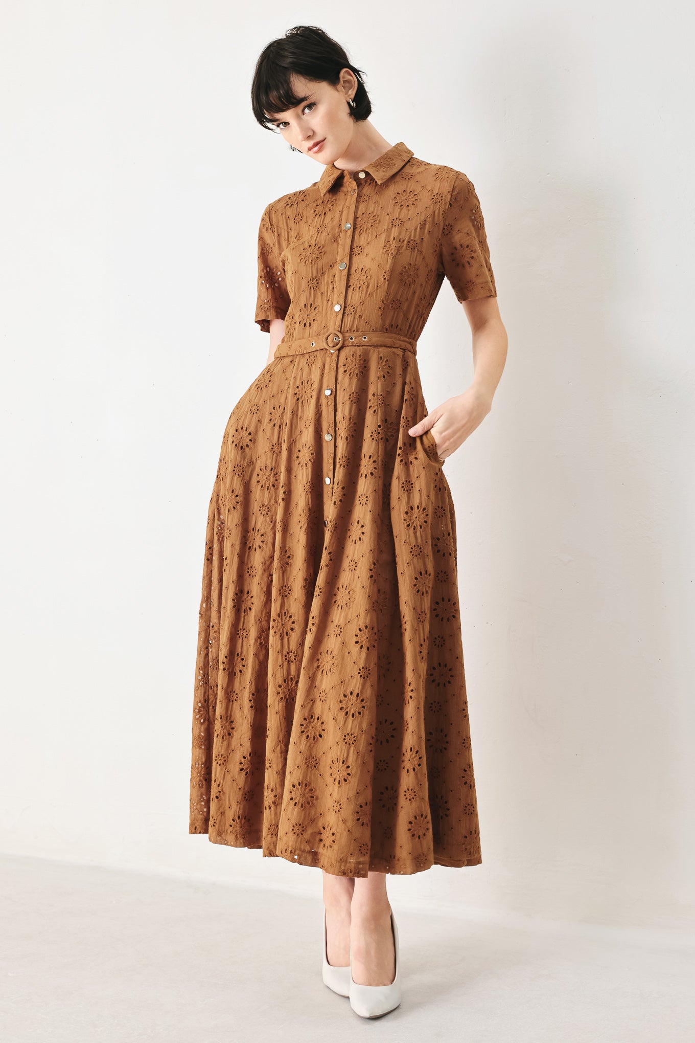 Woman wearing a camel colored eyelet midi dress featuring collar, short sleeve, front button closure, self belt, side pockets and full skirt | FREEMARKET