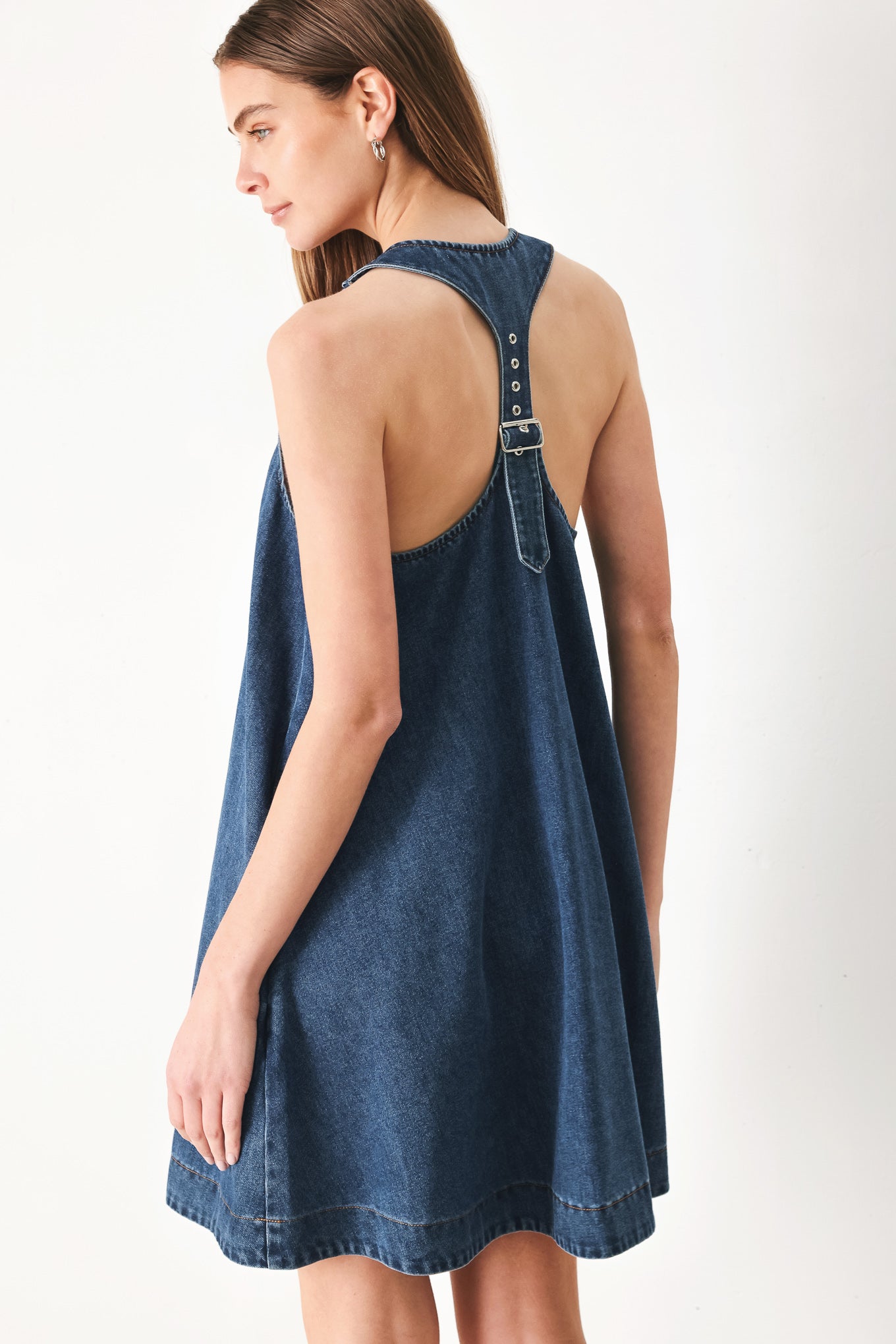 Woman wearing a blue denim mini dress with halter neckline and racer back and buckle | FREEMARKET | Flying Tomato