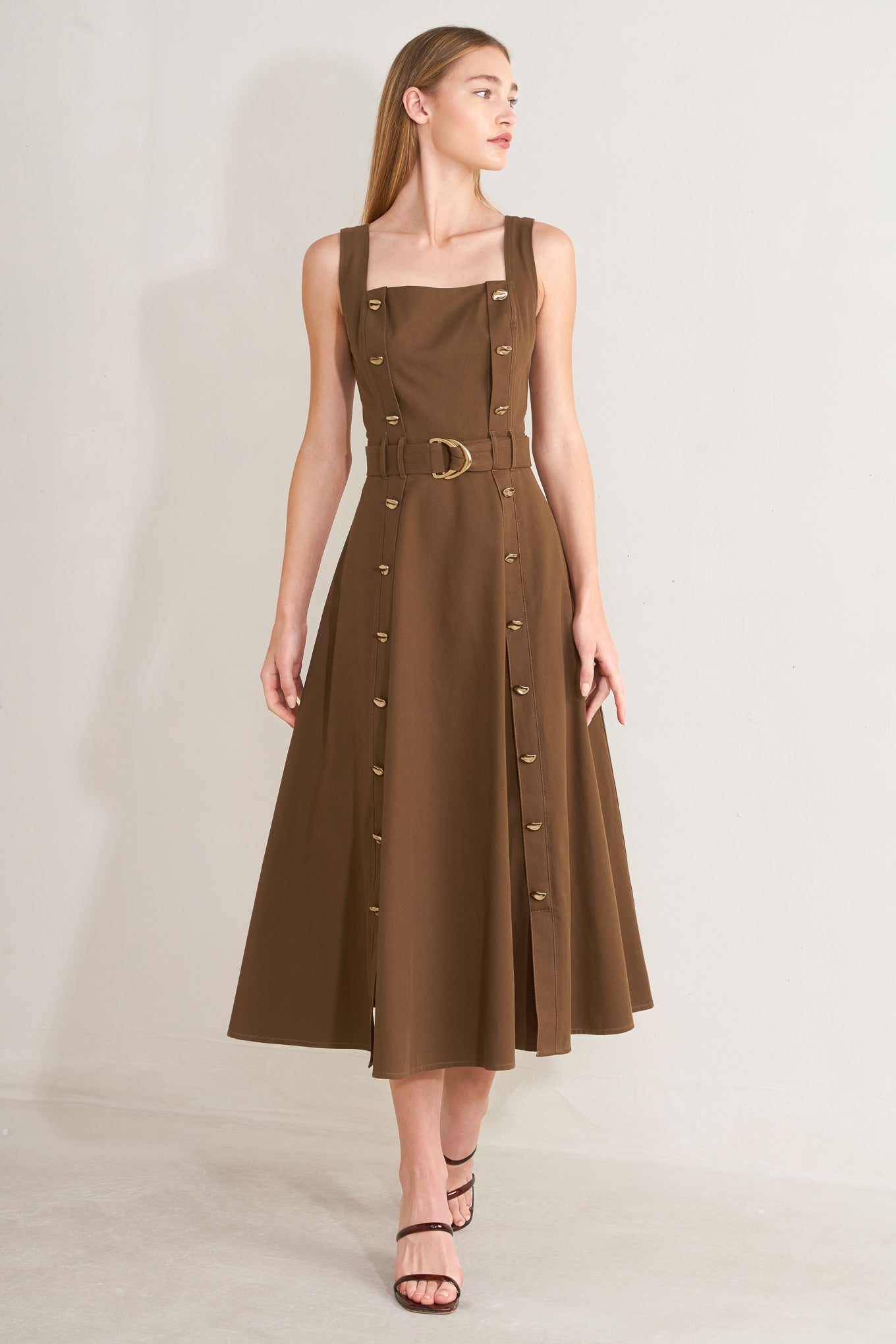 Woman wearing a brown solid woven midi dress featuring straight neckline, straps, button down detail, self belt, circle skirt and back zipper closure with a belt on a plain background | FREEMARKET | Flying Tomato