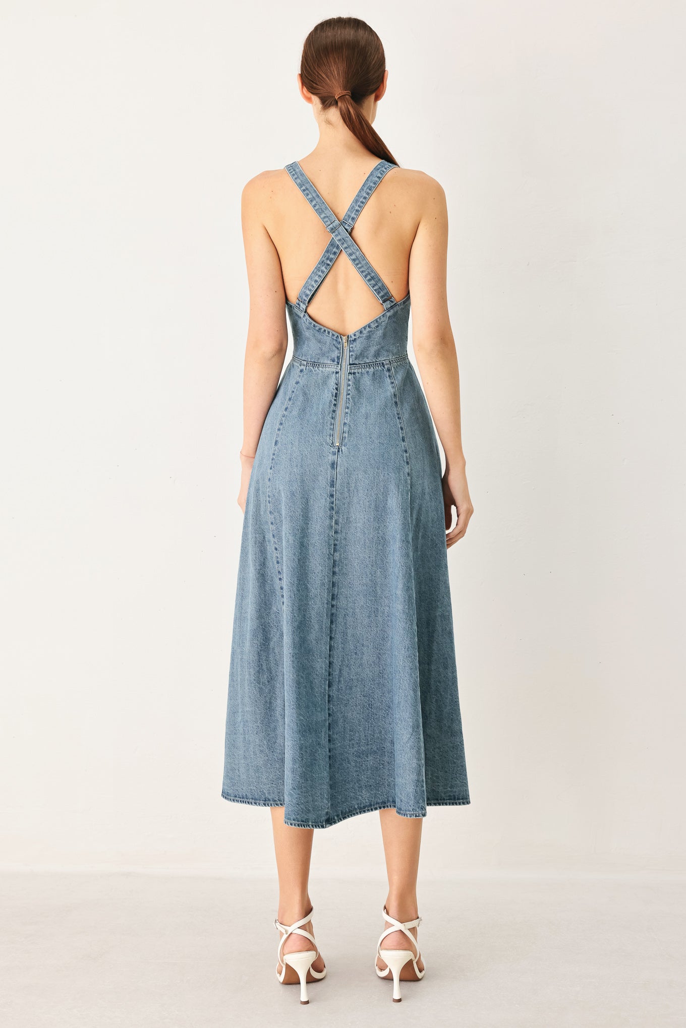Woman wearing a blue denim midi dress featuring V neckline with hardware, circle skirt, bare back with cross strap and zipper closure | FREEMARKET