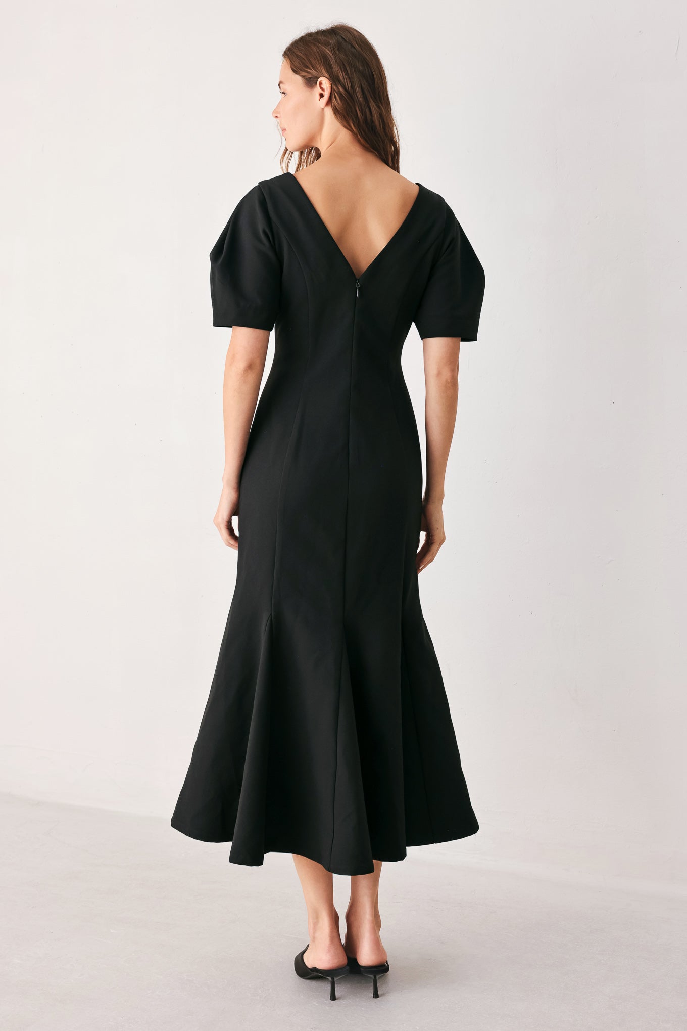 A woman wearing a black midi dress with short puff sleeves, a V-neckline, and a flared hem | FREEMARKET