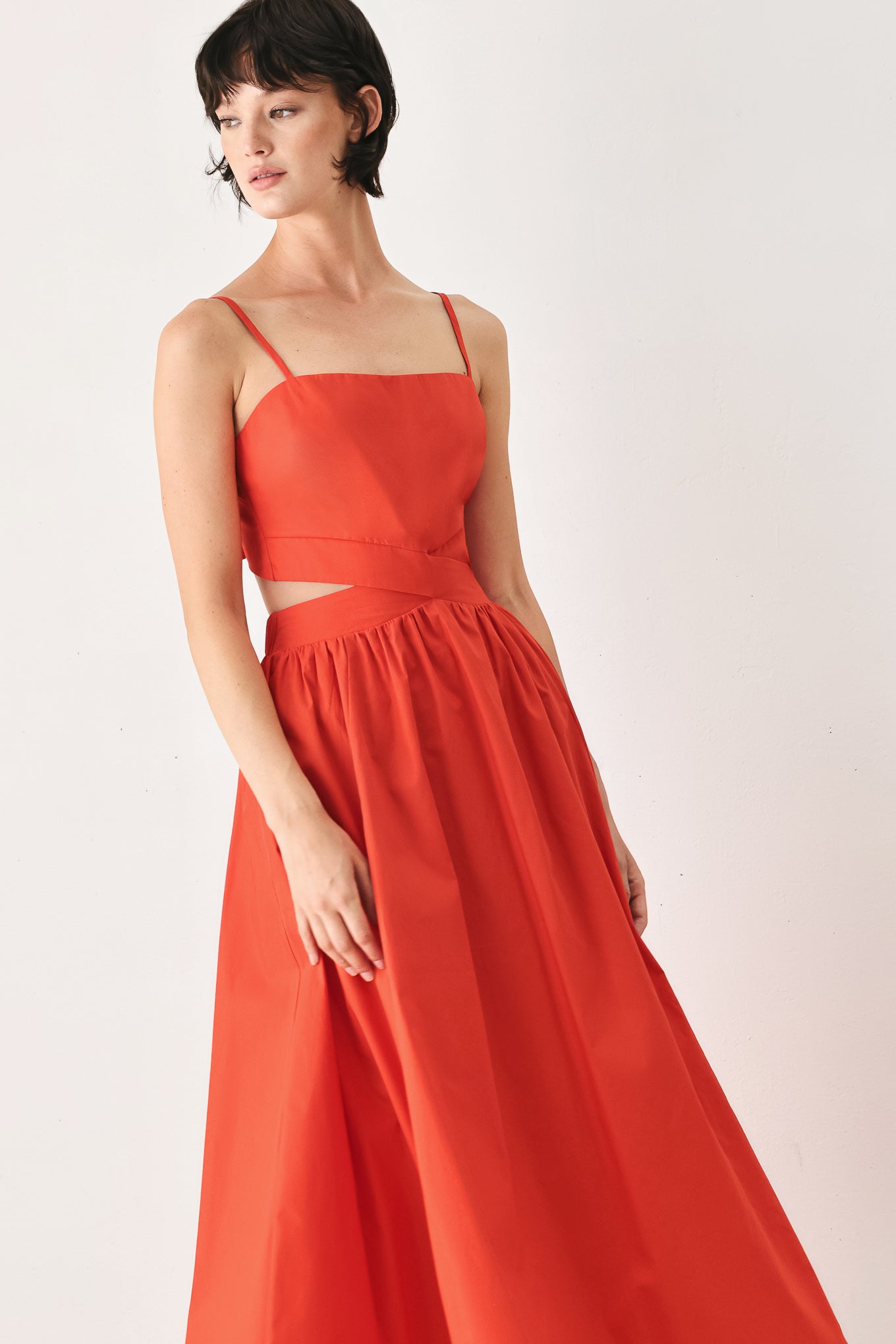 Woman wearing a red midi dress featuring straight neckline, straps, waist cutout, full skirt, and tie detail | FREEMARKET