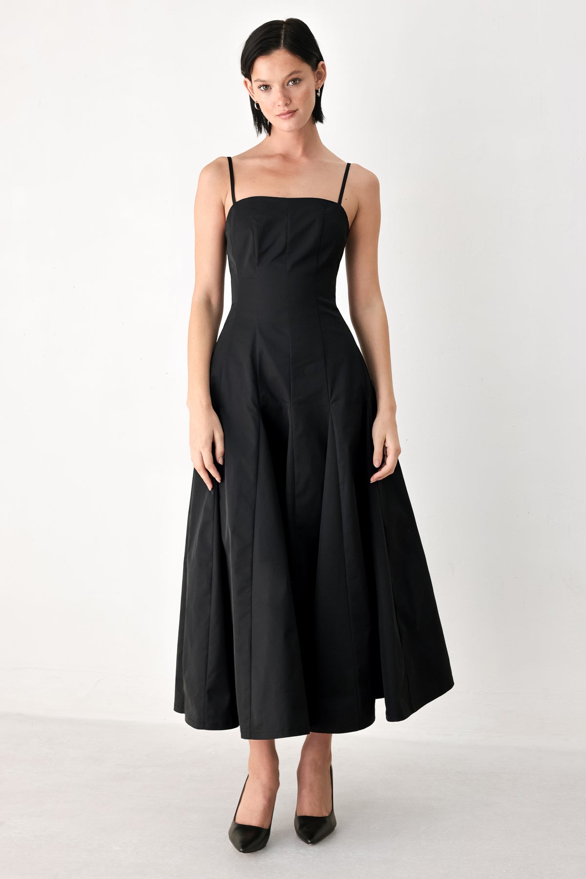 A woman modeling a black midi dress with thin spaghetti straps, a structured square neckline, and a flared skirt | FREEMARKET
