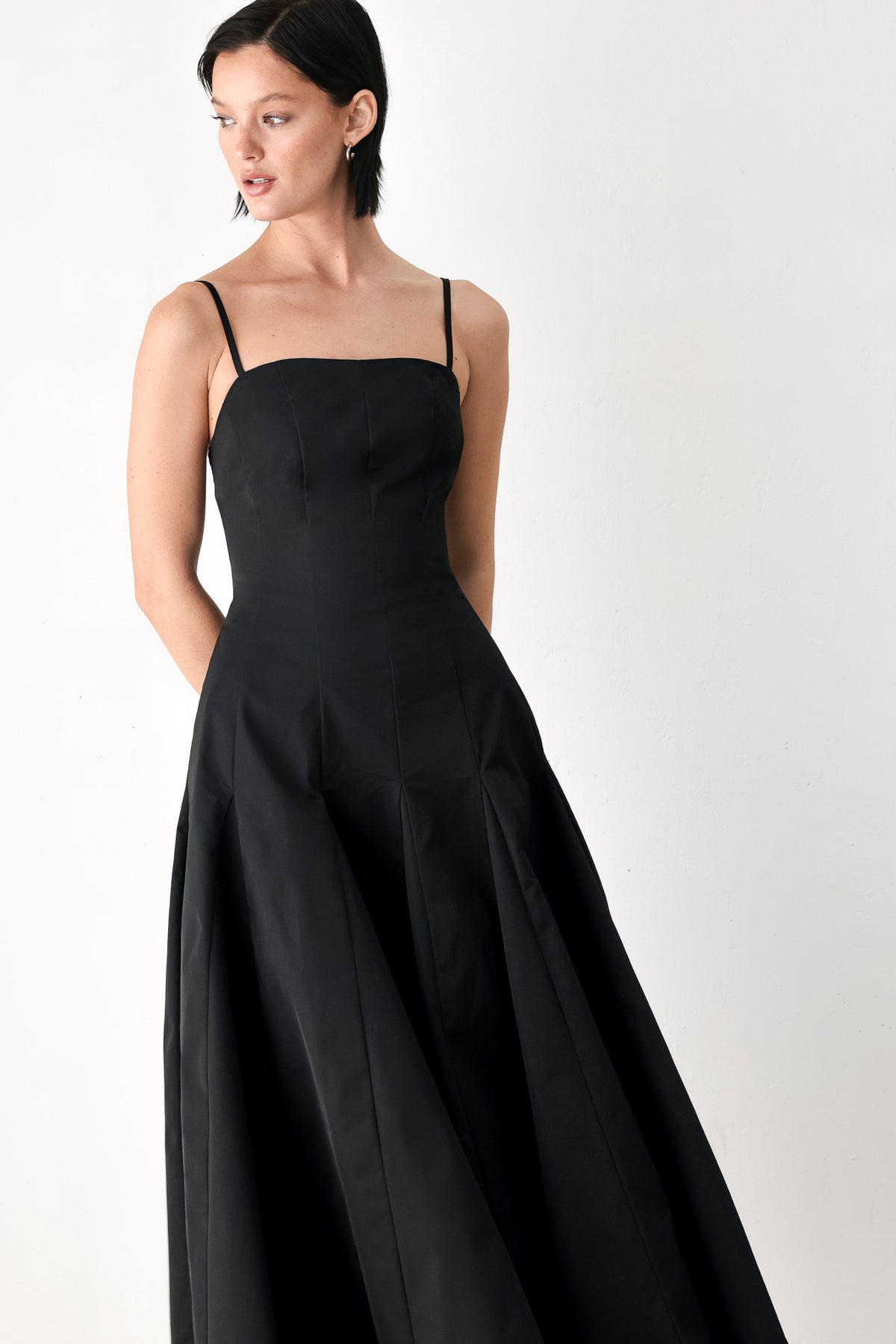 A woman modeling a black midi dress with thin spaghetti straps, a structured square neckline, and a flared skirt | FREEMARKET