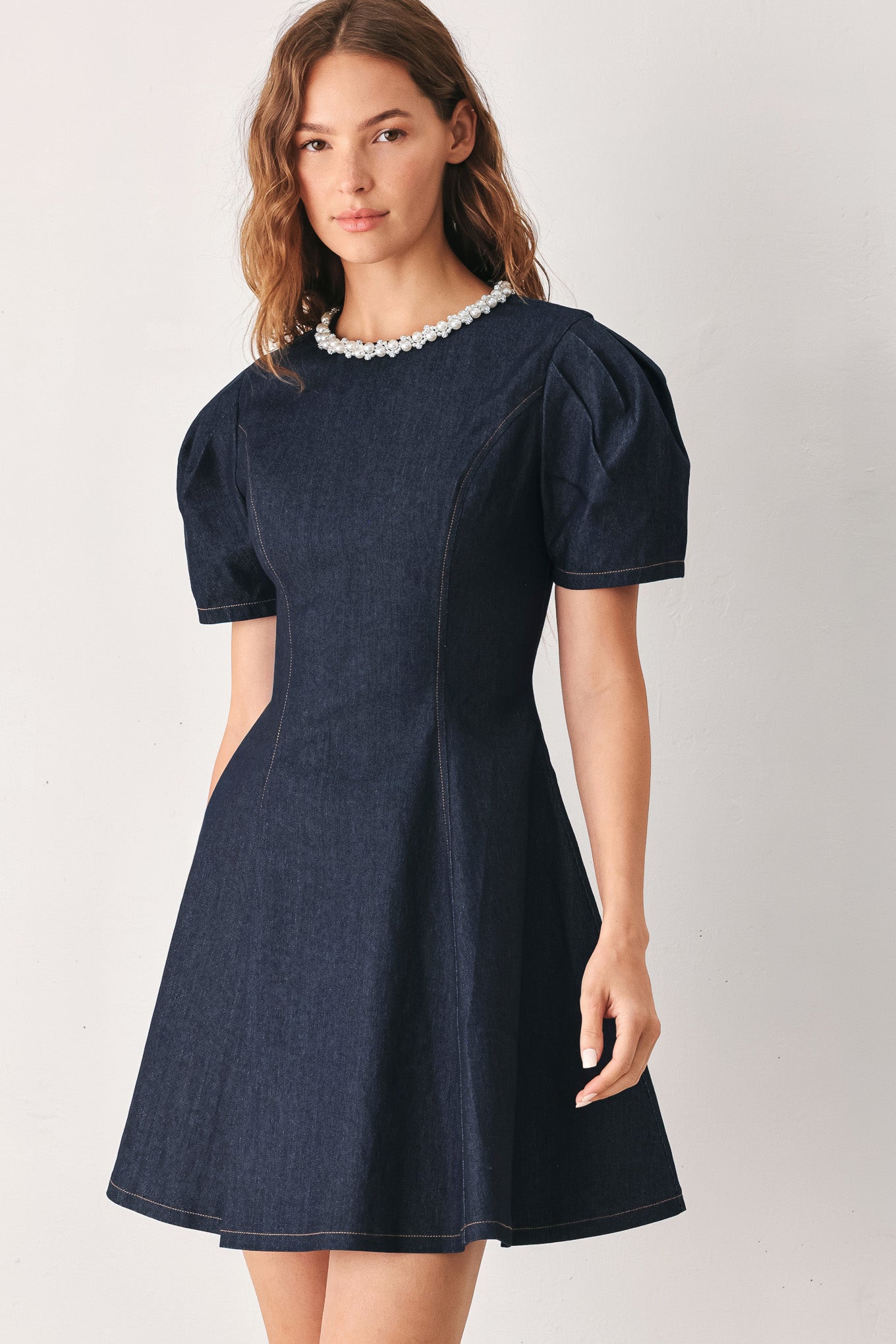 A woman wearing a dark navy blue mini dress with short puff sleeves, a round neckline accented with a white pearl collar, and a flared skirt | FREEMARKET