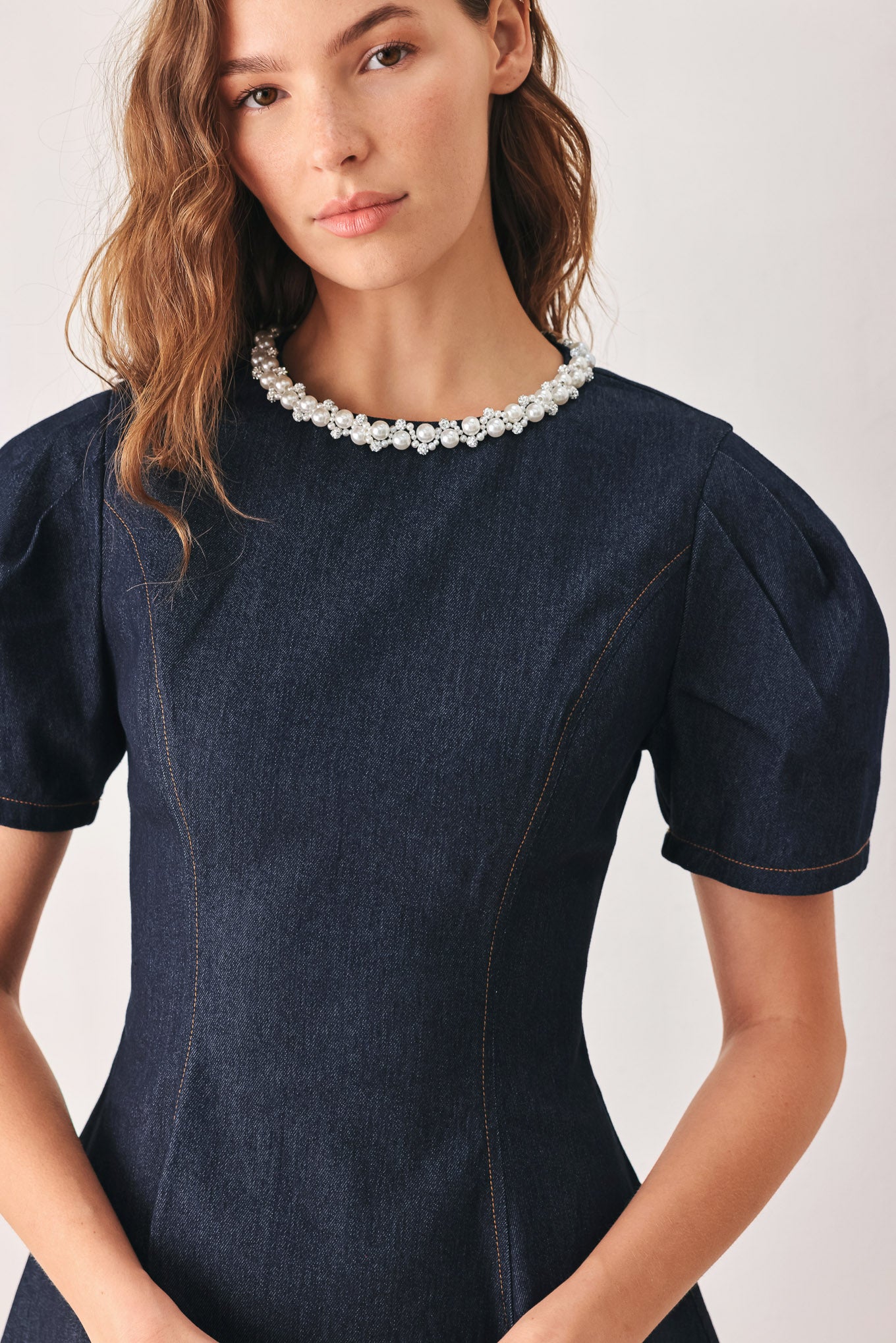 A woman wearing a dark navy blue mini dress with short puff sleeves, a round neckline accented with a white pearl collar, and a flared skirt | FREEMARKET