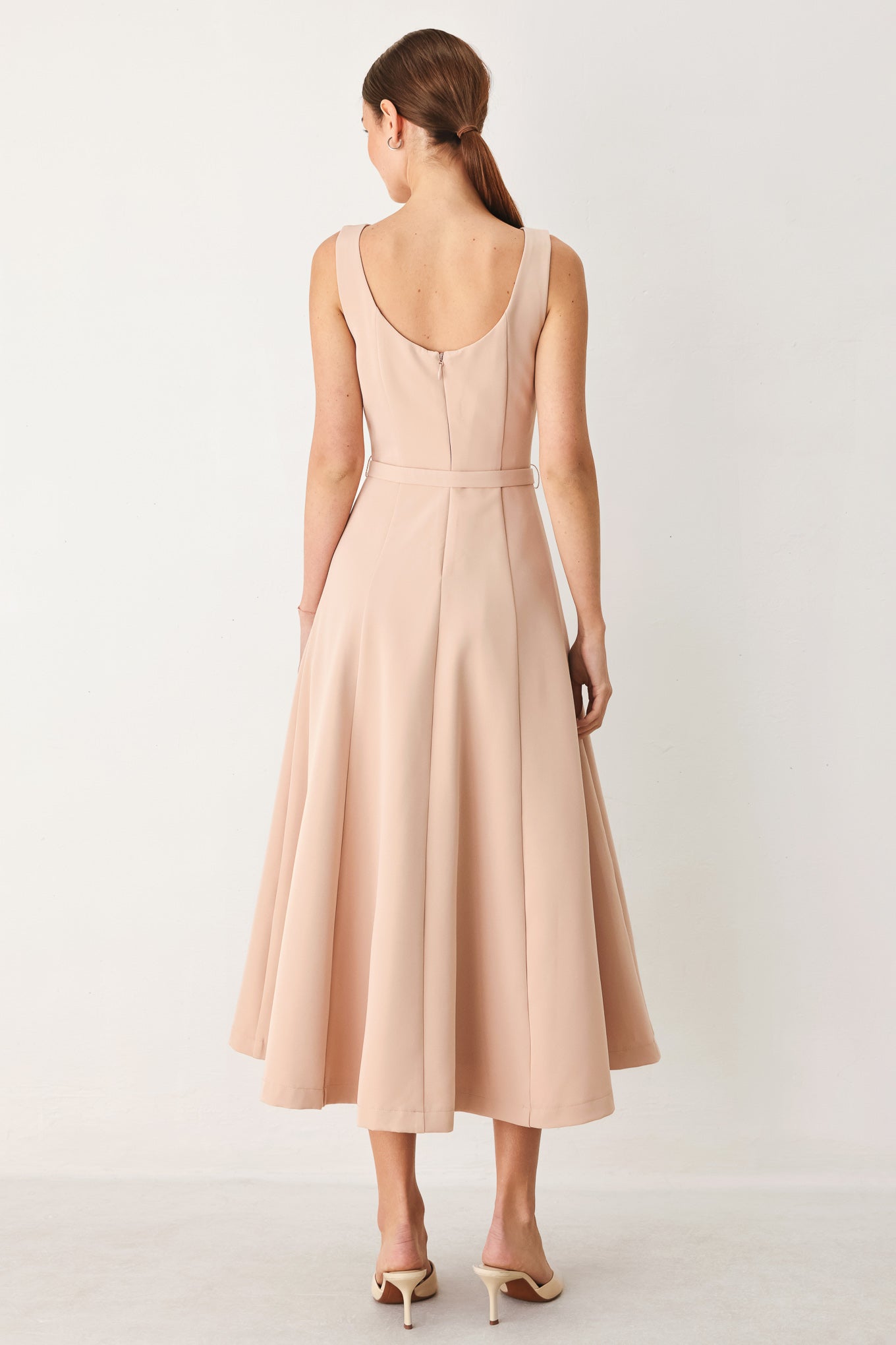 Woman wearing a sleeveless soft blush midi dress featuring boat neckline, circle skirt, self belt and back zipper closure | FREEMARKET