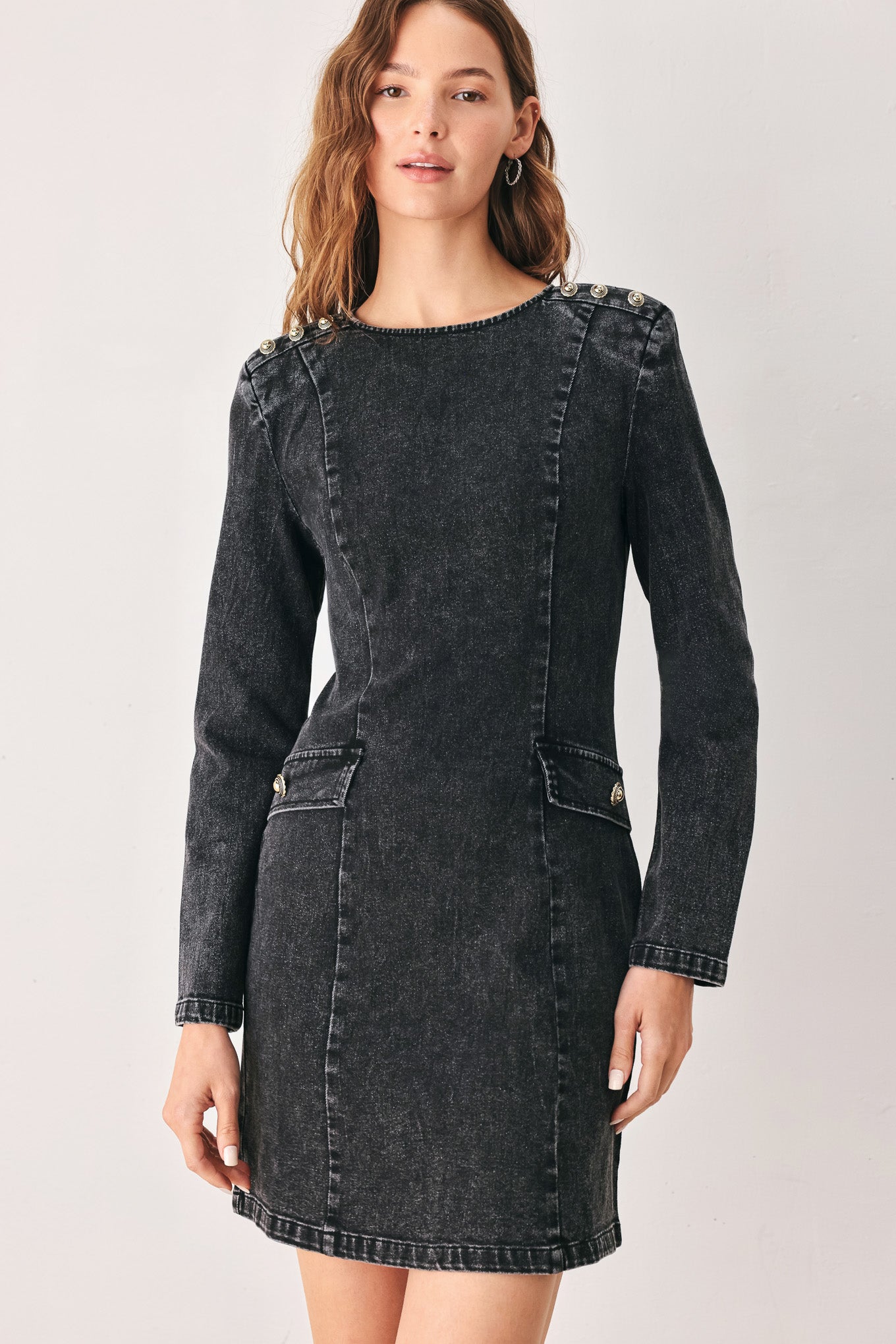 A woman wearing a dark black washed denim mini dress with shoulder embellishments and front patch pockets | FREEMARKET