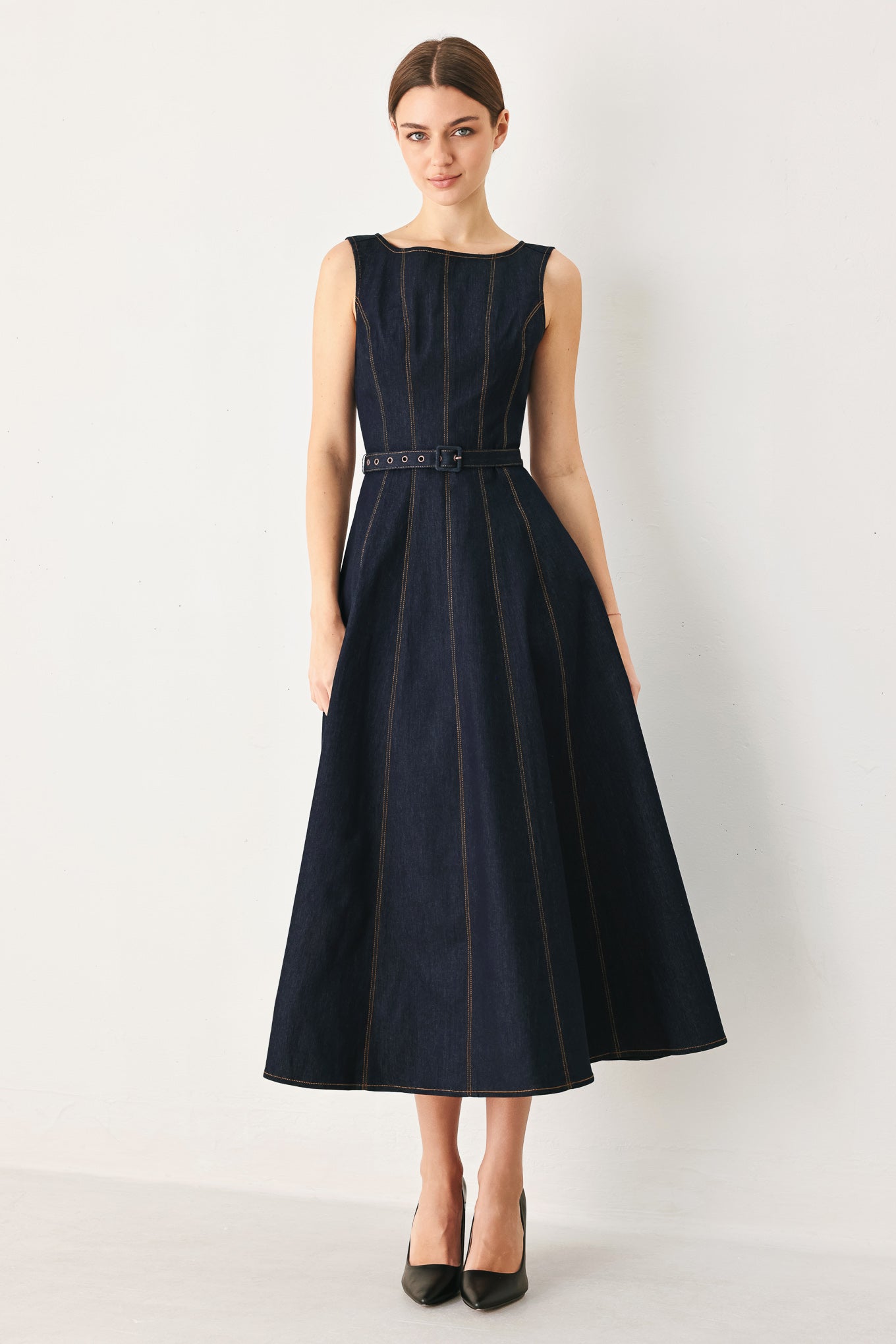 Woman wearing a dark denim sleeveless midi dress featuring wide neckline, self belt, full circle skirt and back zipper closure | FREEMARKET